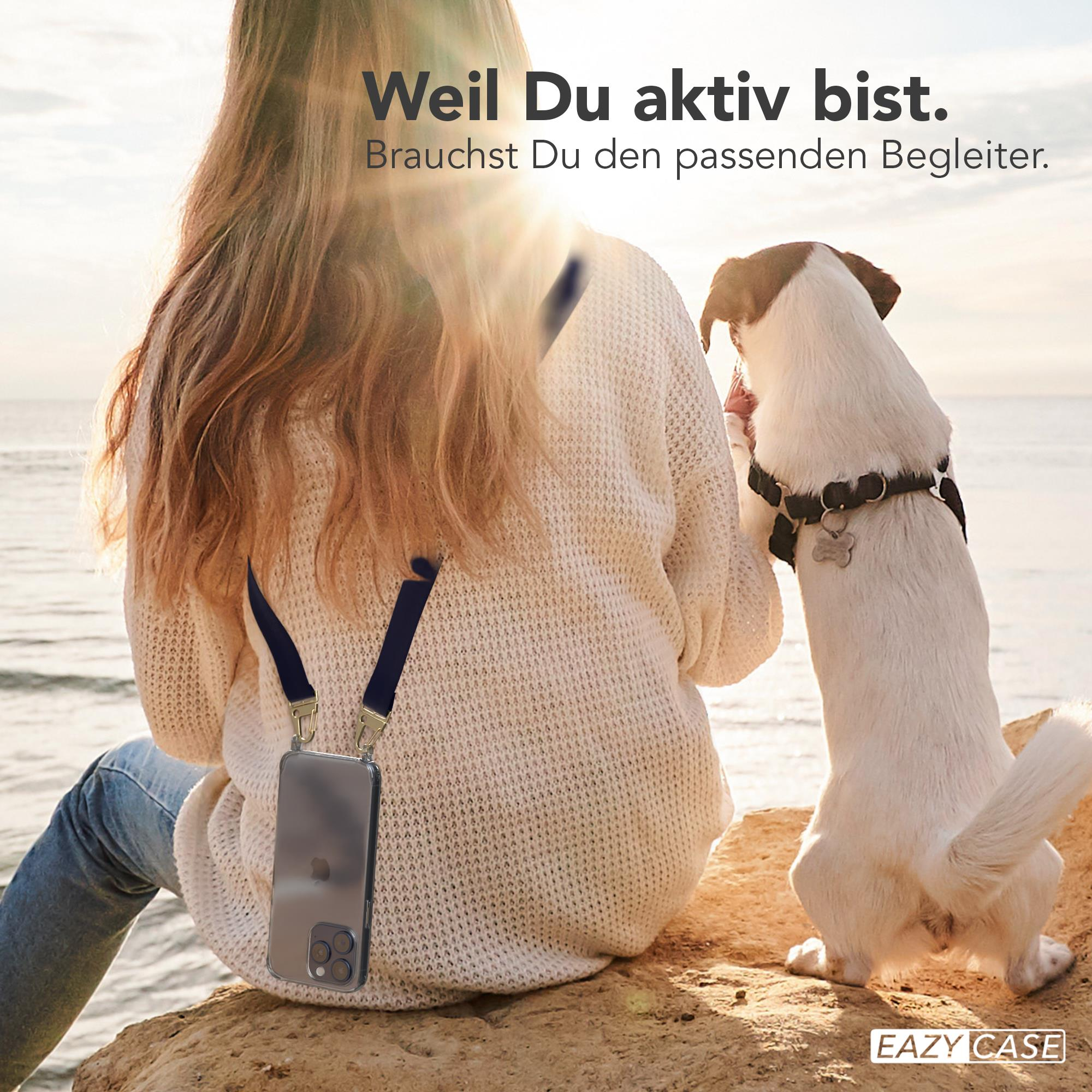 Eine Frau mit einem Telefon an einem Riemen und ein Hund am Strand. Das Telefon hängt an ihrer Brust.