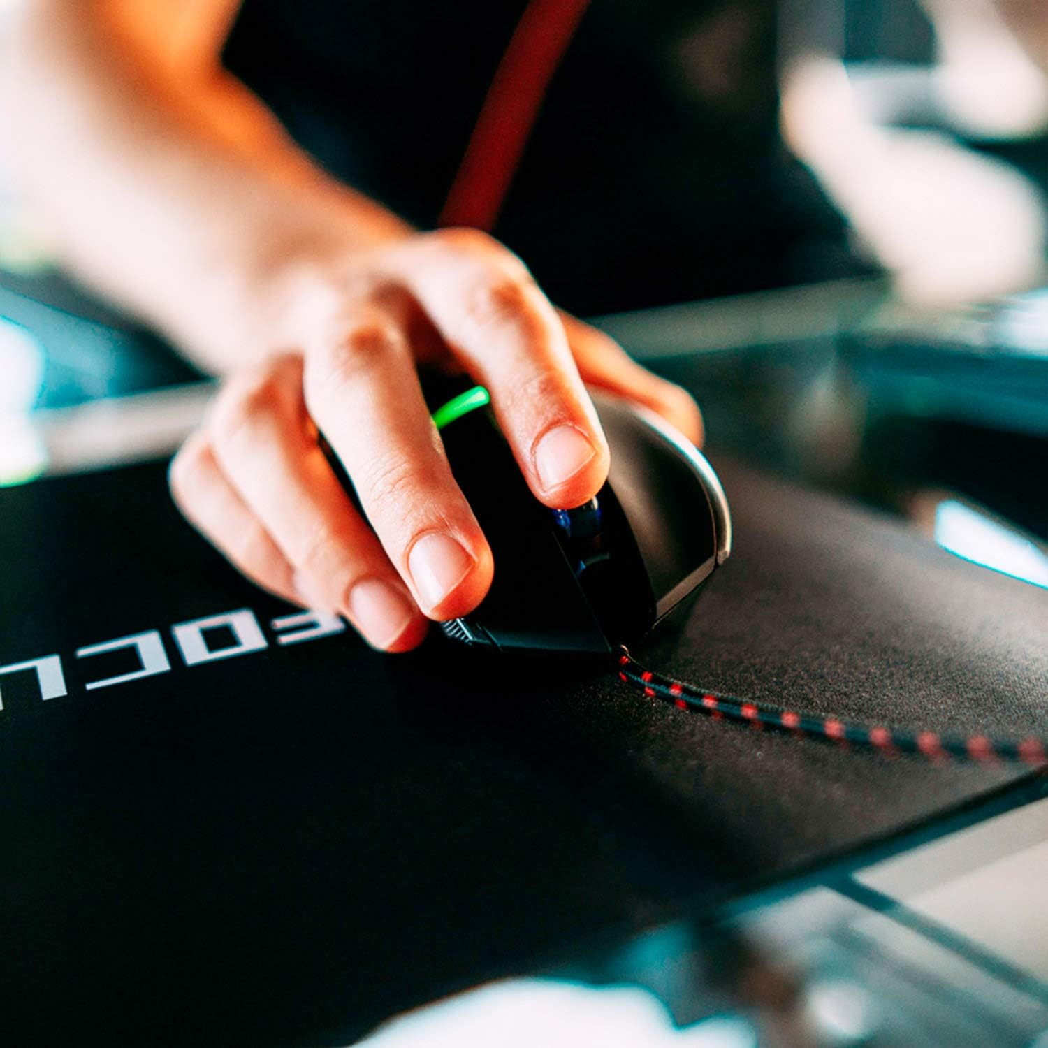 Die Hand einer Person, die eine schwarze Gaming-Maus auf einem schwarzen Mauspads mit weißem Text hält.