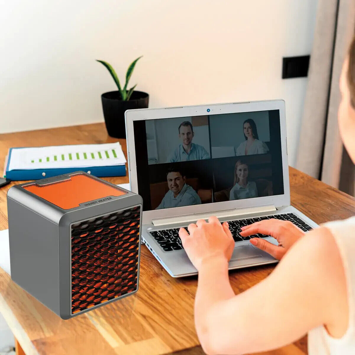 Una persona usando una laptop, con una videollamada en la pantalla y un pequeño calefactor en el escritorio.