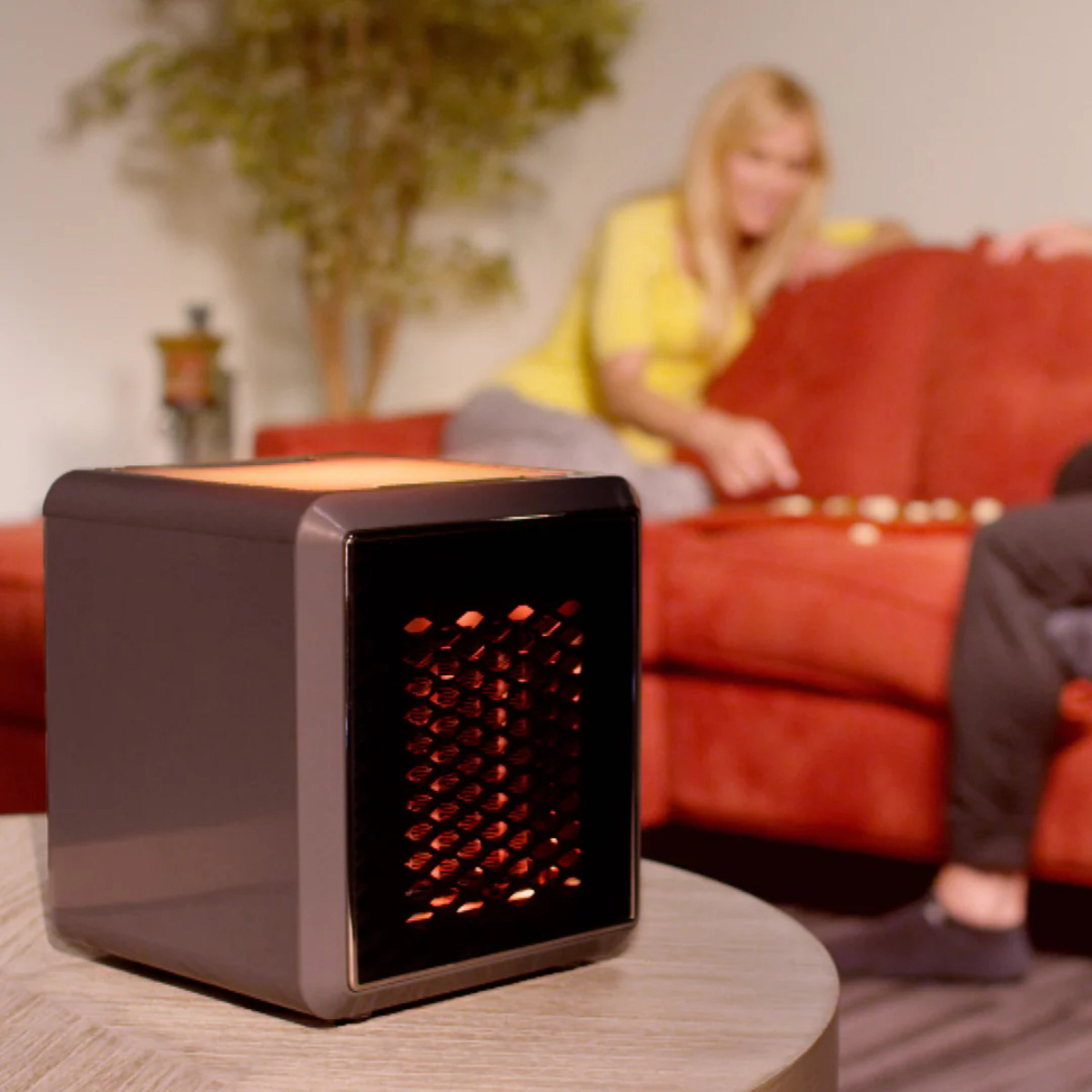 Un calefactor en forma de cubo sobre una mesa. Una pareja está sentada y jugando un juego de mesa en el fondo.