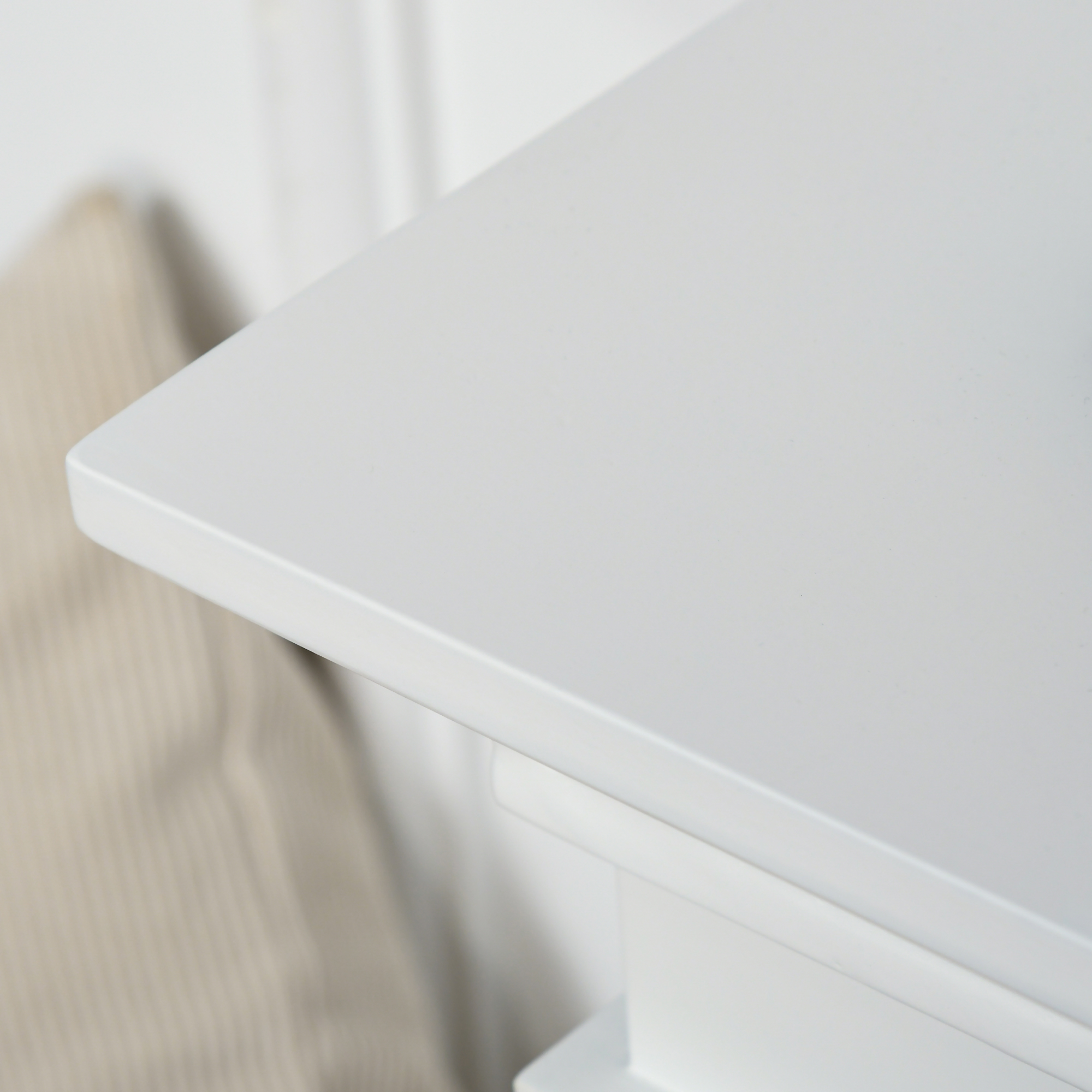 Primer plano de una esquina de mesa blanca con borde redondeado. Almohada crema y pared blanca al fondo.