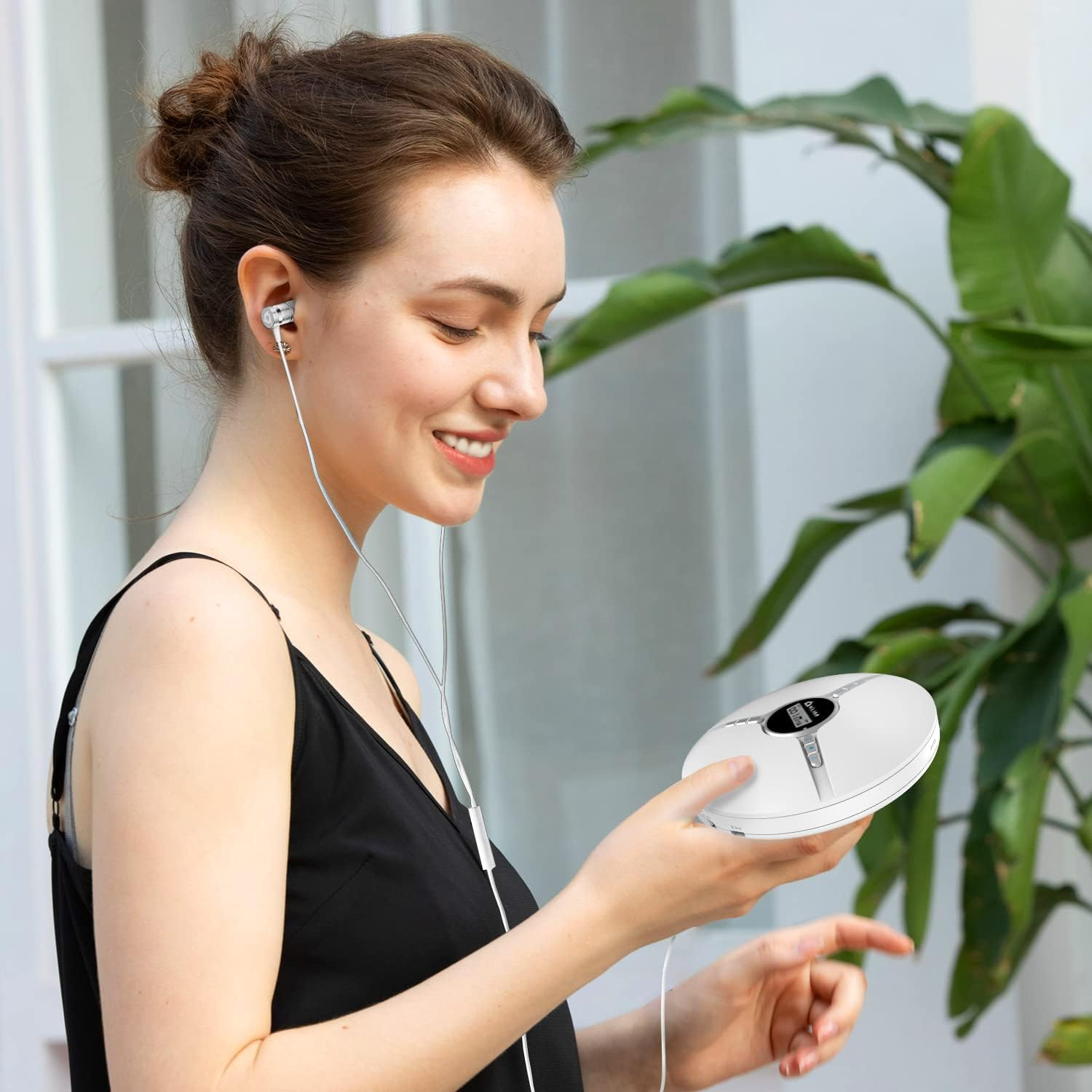 Frau mit Kopfhörern hält weißen tragbaren CD-Player, lächelt in der Nähe von Pflanzen.