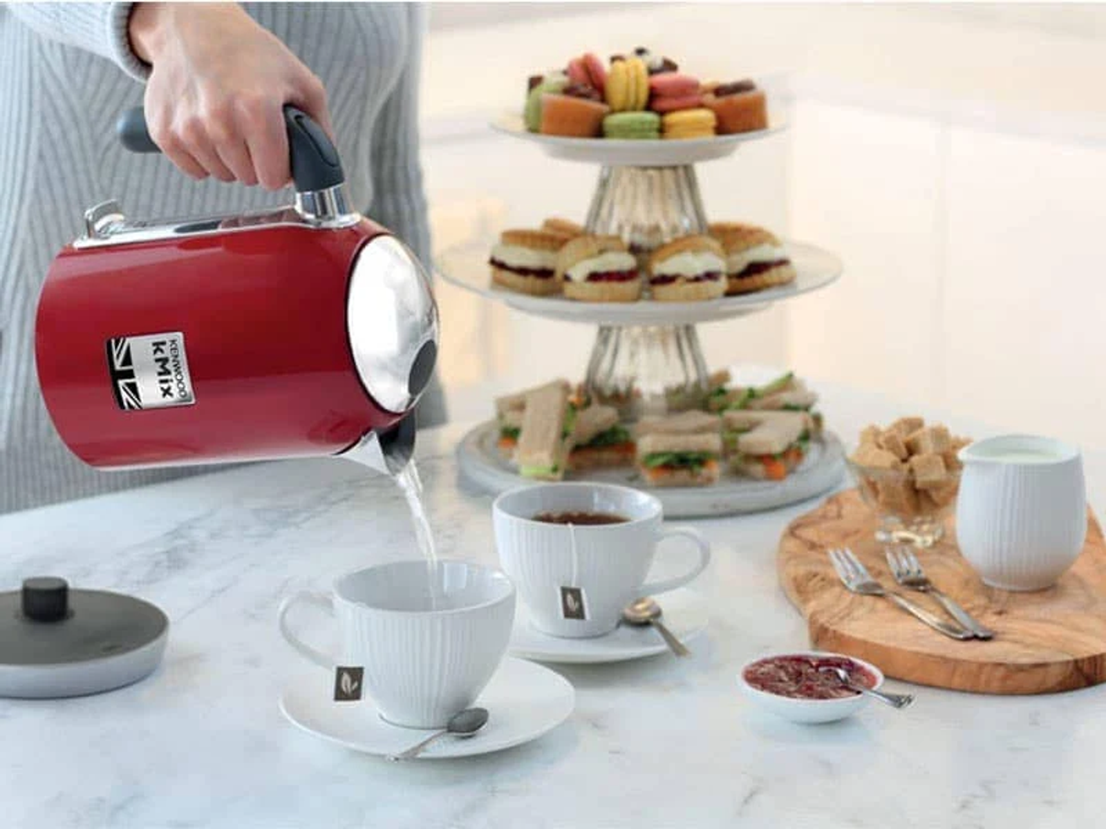 Czerwony czajnik nalewa wodę do dwóch białych filiżanek z torebkami herbaty i smakołykami.