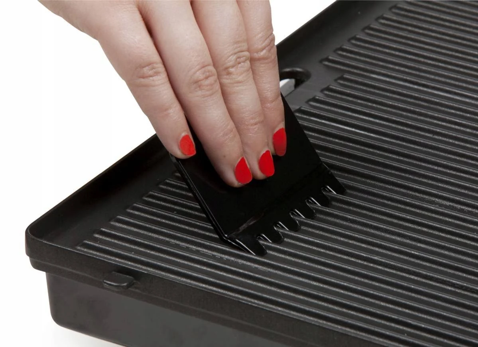 Ręka z czerwonymi paznokciami czyści czarny grill skrobakiem.