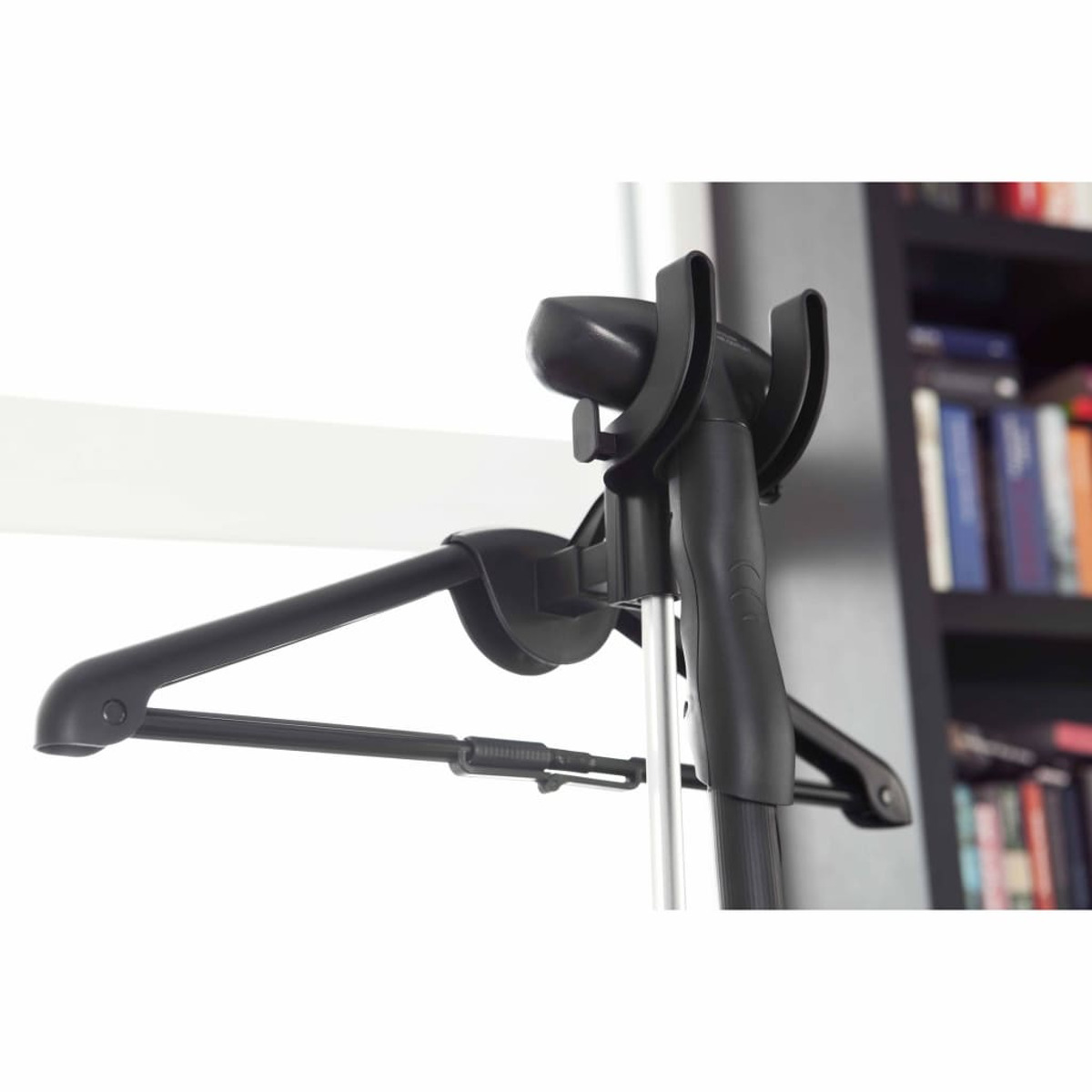 Vaporizador de ropa negro con una percha en una habitación con estantería.