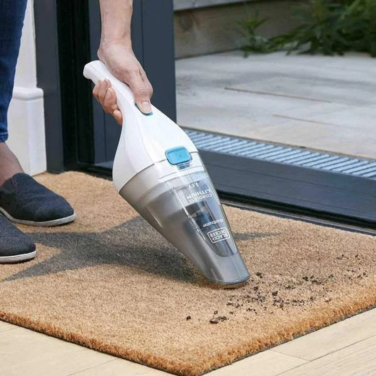 Osoba odkurzająca dywan, z czarno-białym odkurzaczem.