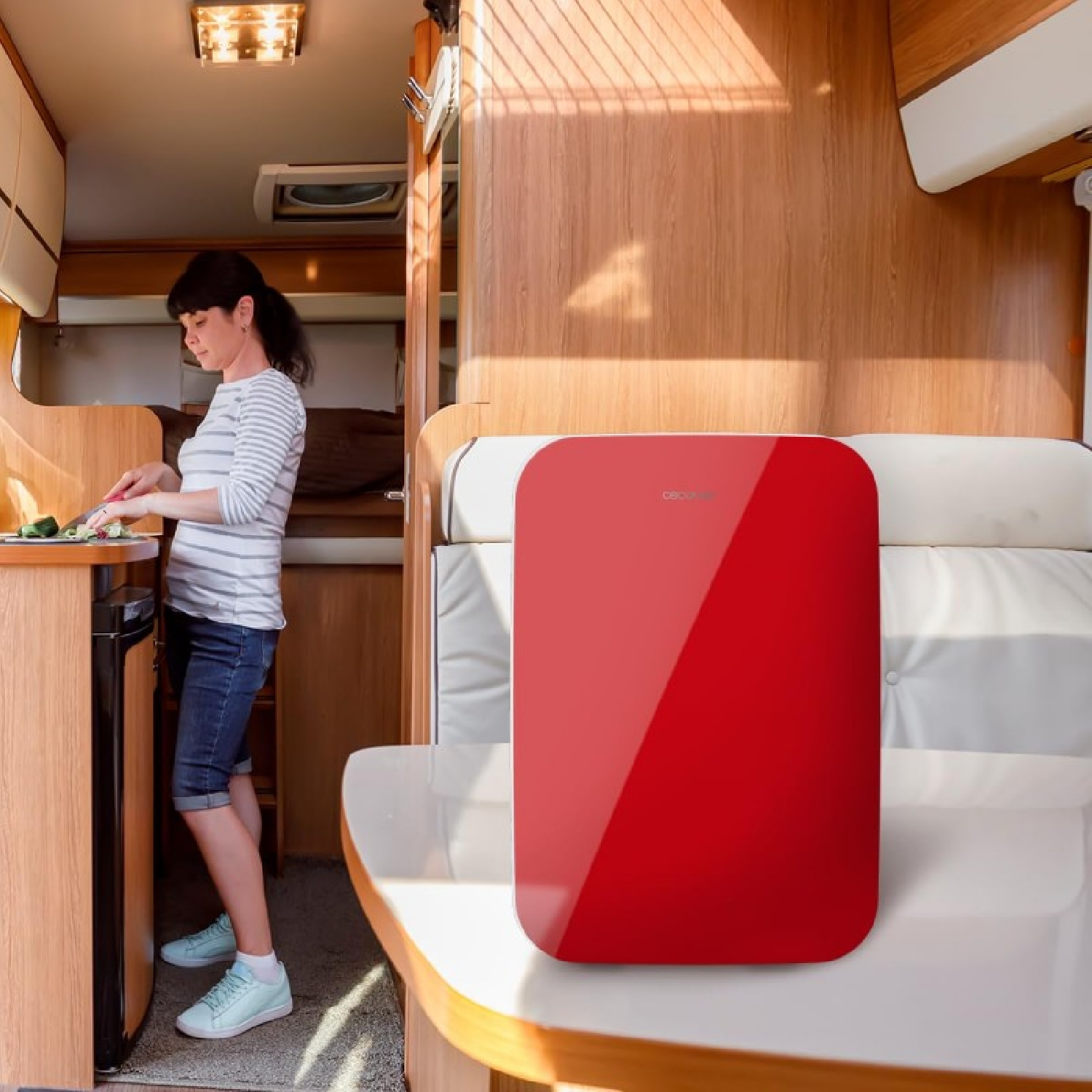 Donna che taglia verdure in una cucina di camper; dispositivo rosso sul tavolo.
