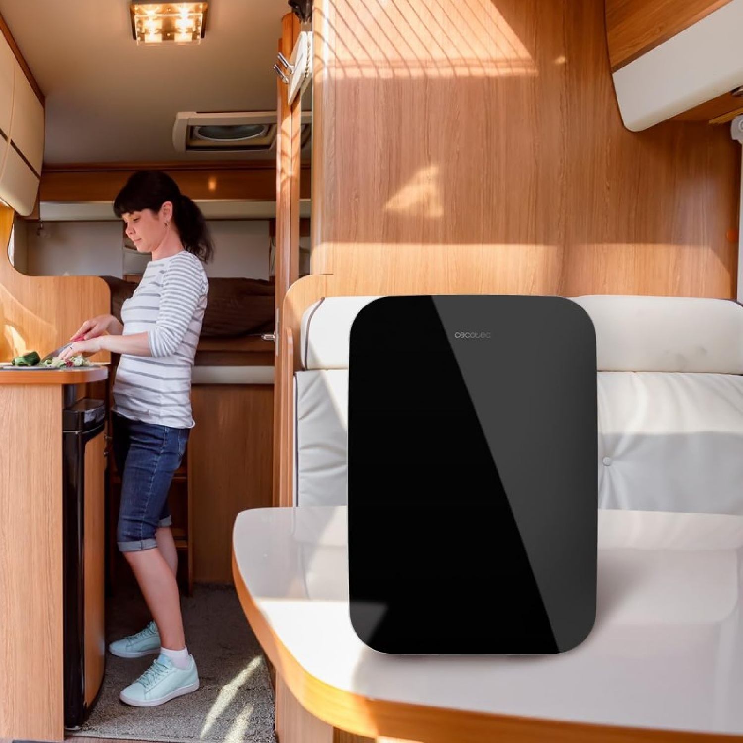 Una mujer está en una autocaravana, cortando verduras. Un electrodoméstico negro y rectangular está sobre una mesa.