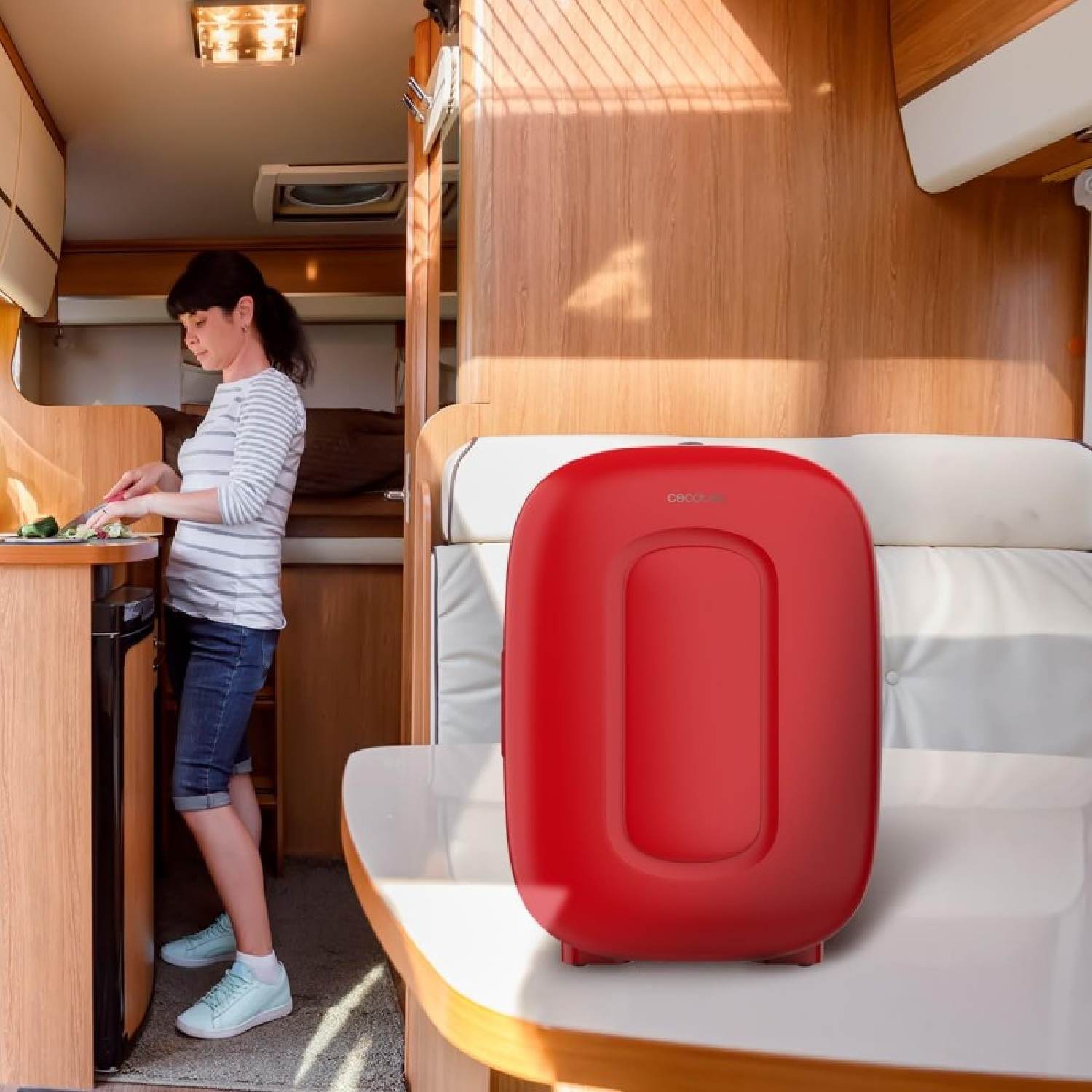 Una donna taglia verdure in un camper. C'è un elettrodomestico rosso a destra.