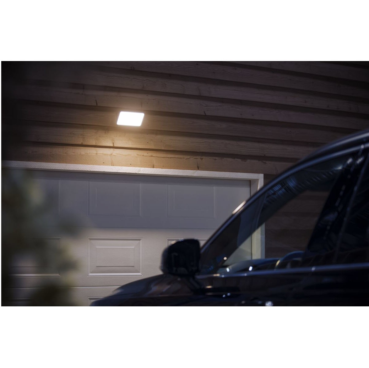 Voiture garée devant un garage la nuit, éclairée par une lumière zénithale carrée.