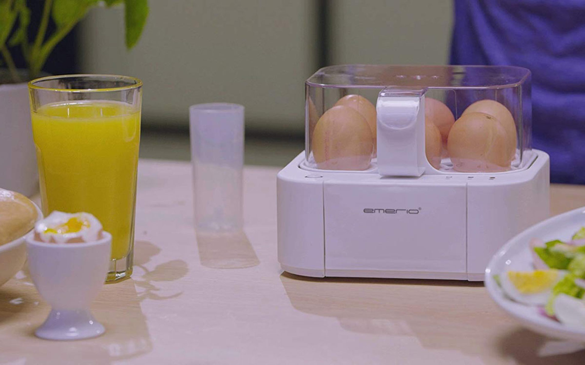 Eier in einem Eierkocher, ein Glas Saft und gekochte Eier auf einem Tisch.