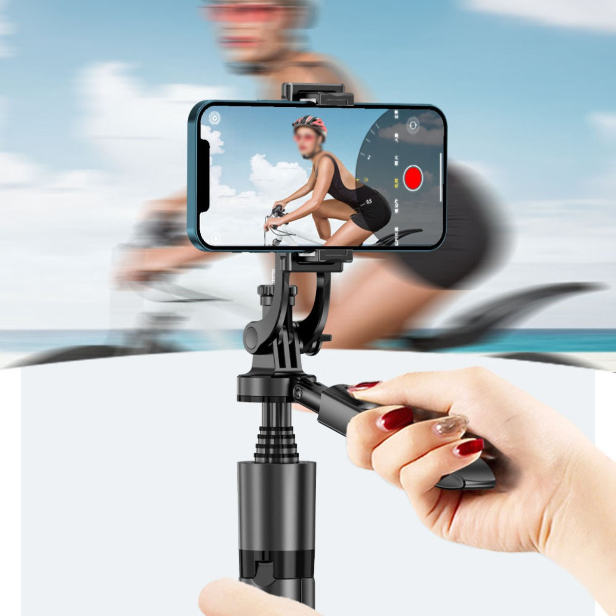 Eine Person hält ein Telefon mit einem Radfahrer auf dem Bildschirm, mit einem Selfie-Stick, am Strand.