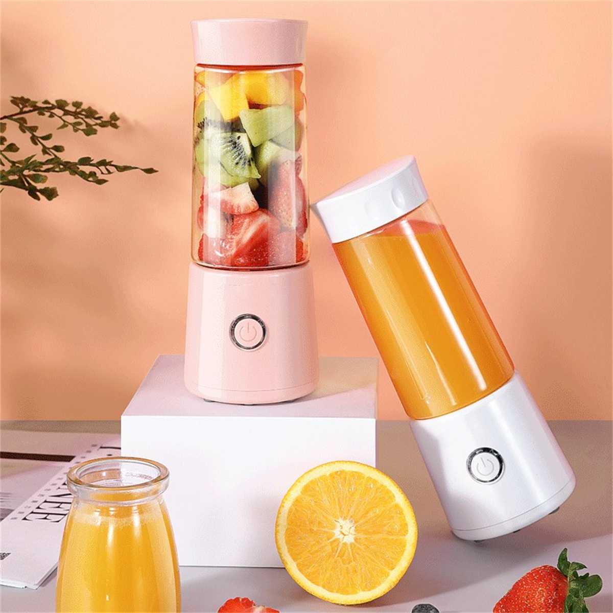 Zwei tragbare Mixer mit Obst. Einer mit Erdbeeren, Kiwi und Mango. Der andere mit Orangensaft.