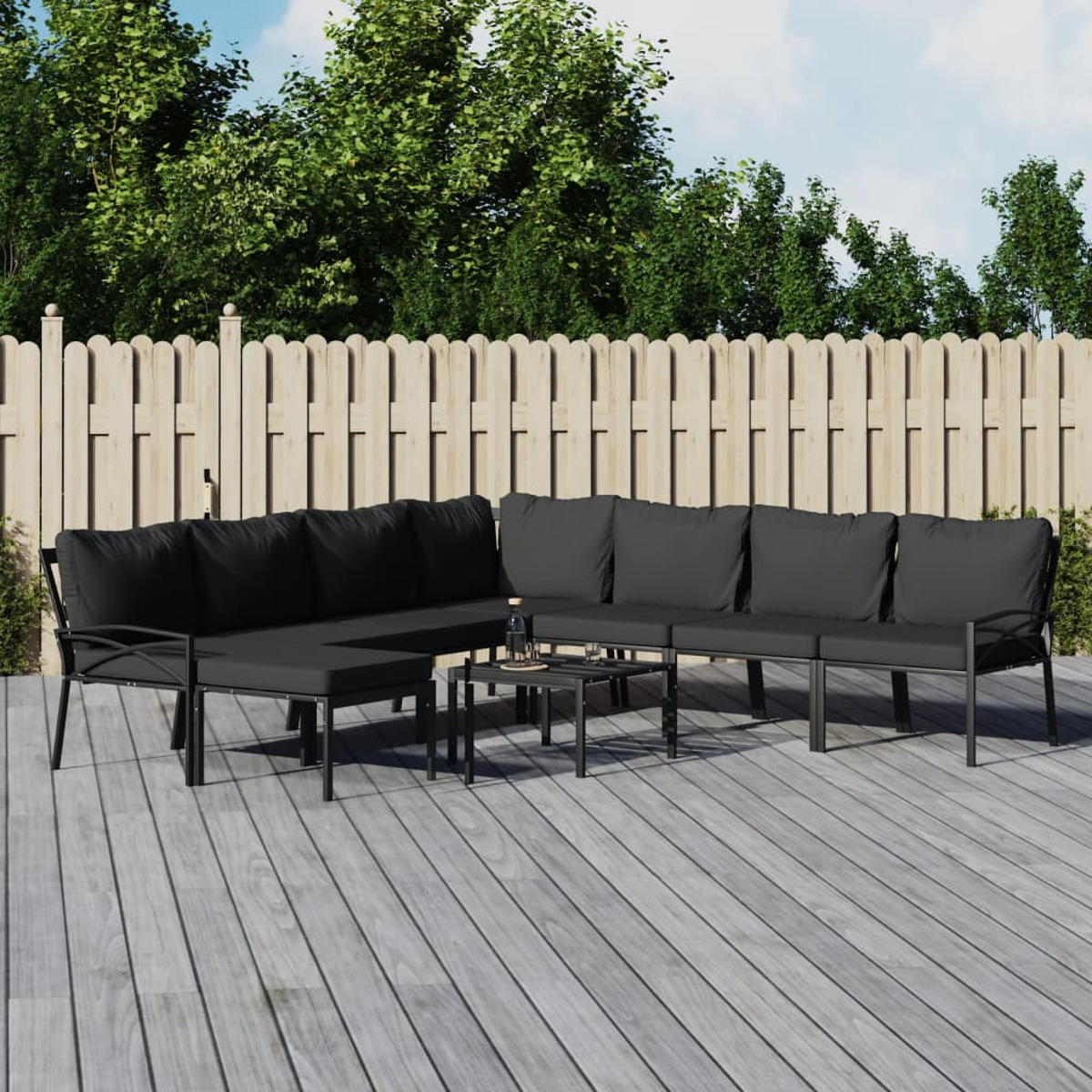 Gartenmöbel-Set. Schwarzes Metallgestell, dunkelgraue Kissen. Holzterrasse und weißer Zaun.