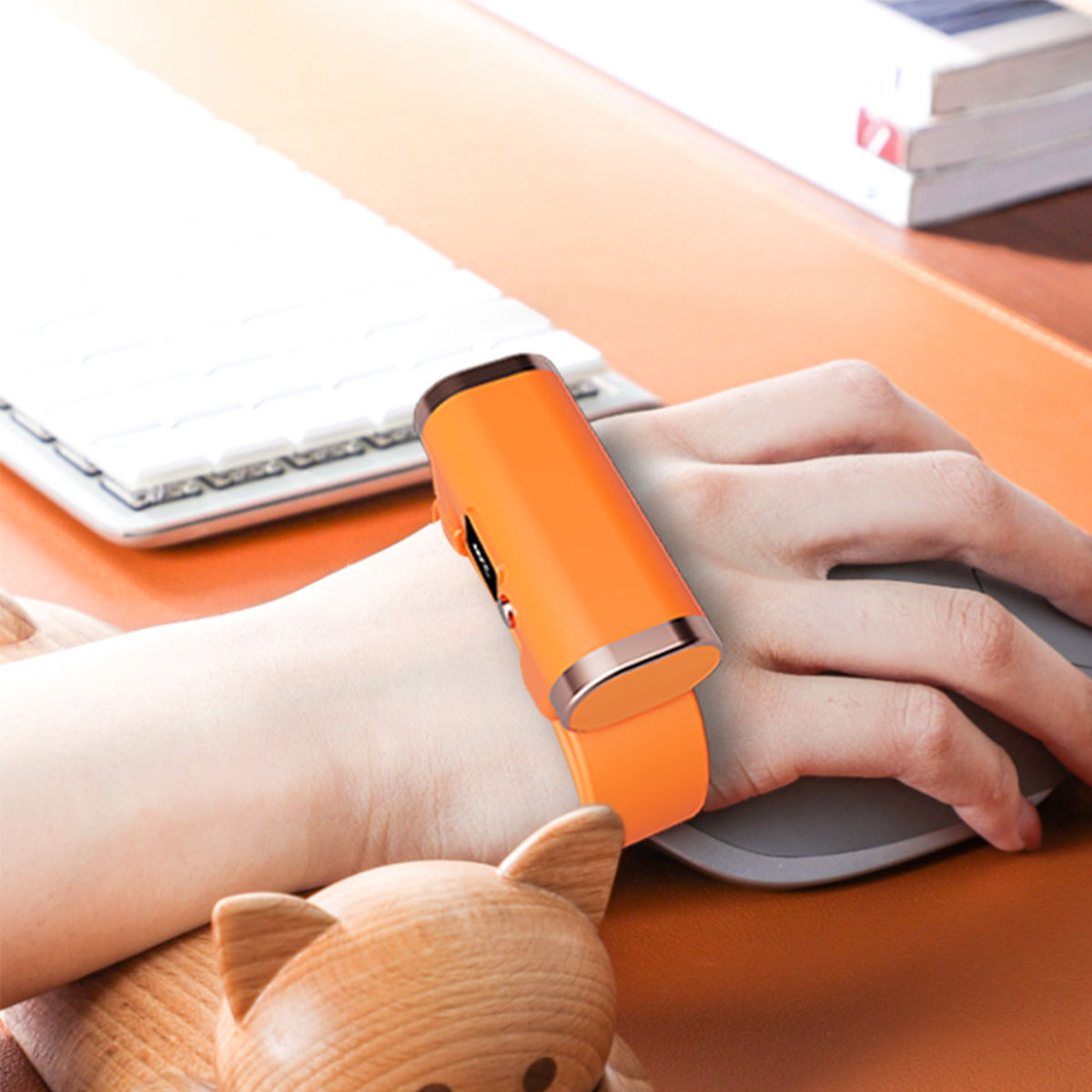 Hand mit orangefarbenem Armband-Maus. Weiße Tastatur im Hintergrund, braune Schreibtischoberfläche.