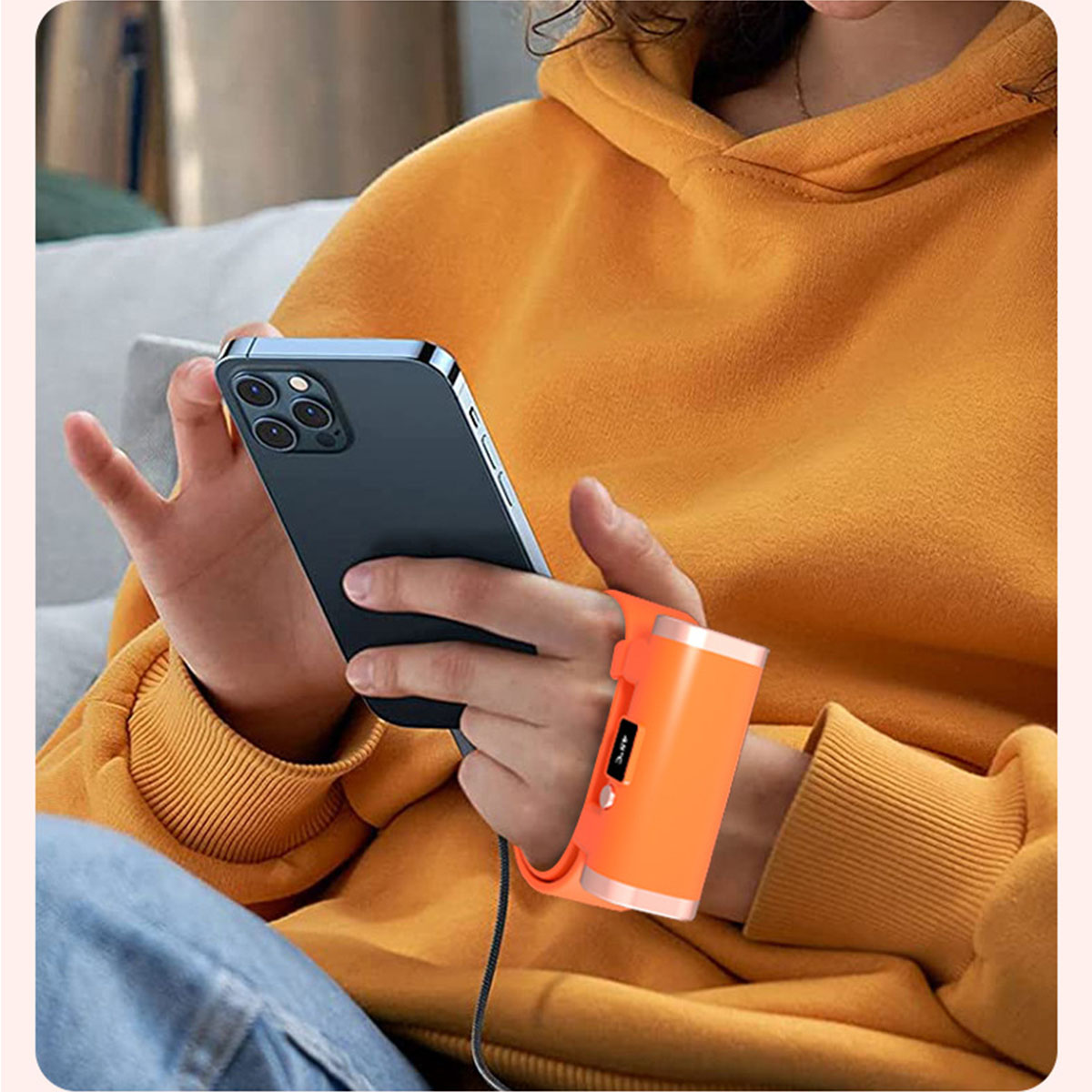 Eine Person, die ein Telefon und einen orangefarbenen tragbaren Heizlüfter hält.
