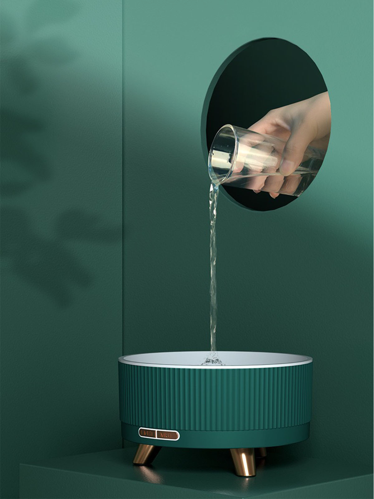Eine Hand gießt Wasser in einen grünen, zylindrischen Wasserspender. Goldakzente am Sockel.