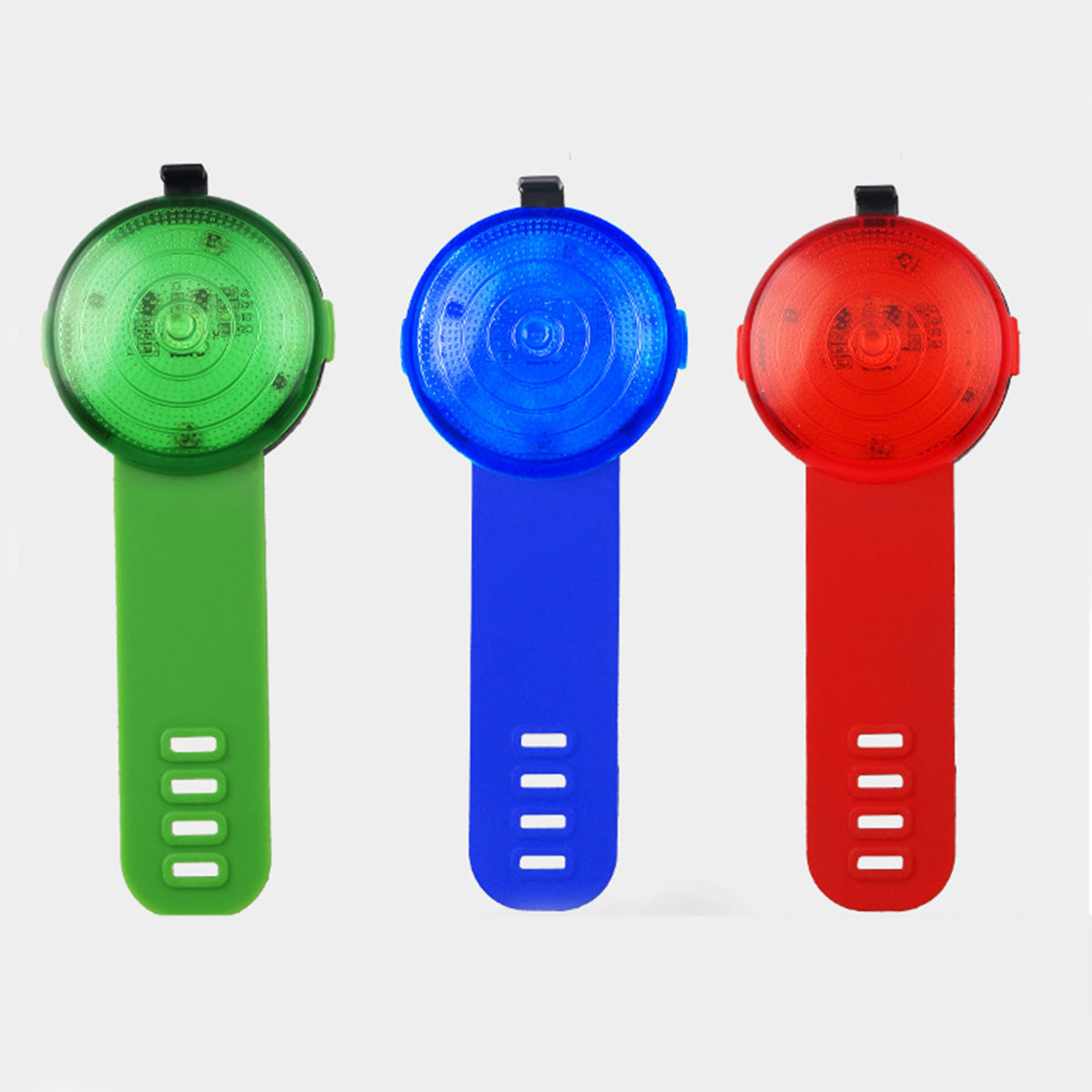 Drei farbige Fahrradlichter: grün, blau und rot, mit schwarzen Oberteilen und farbigen Riemen.