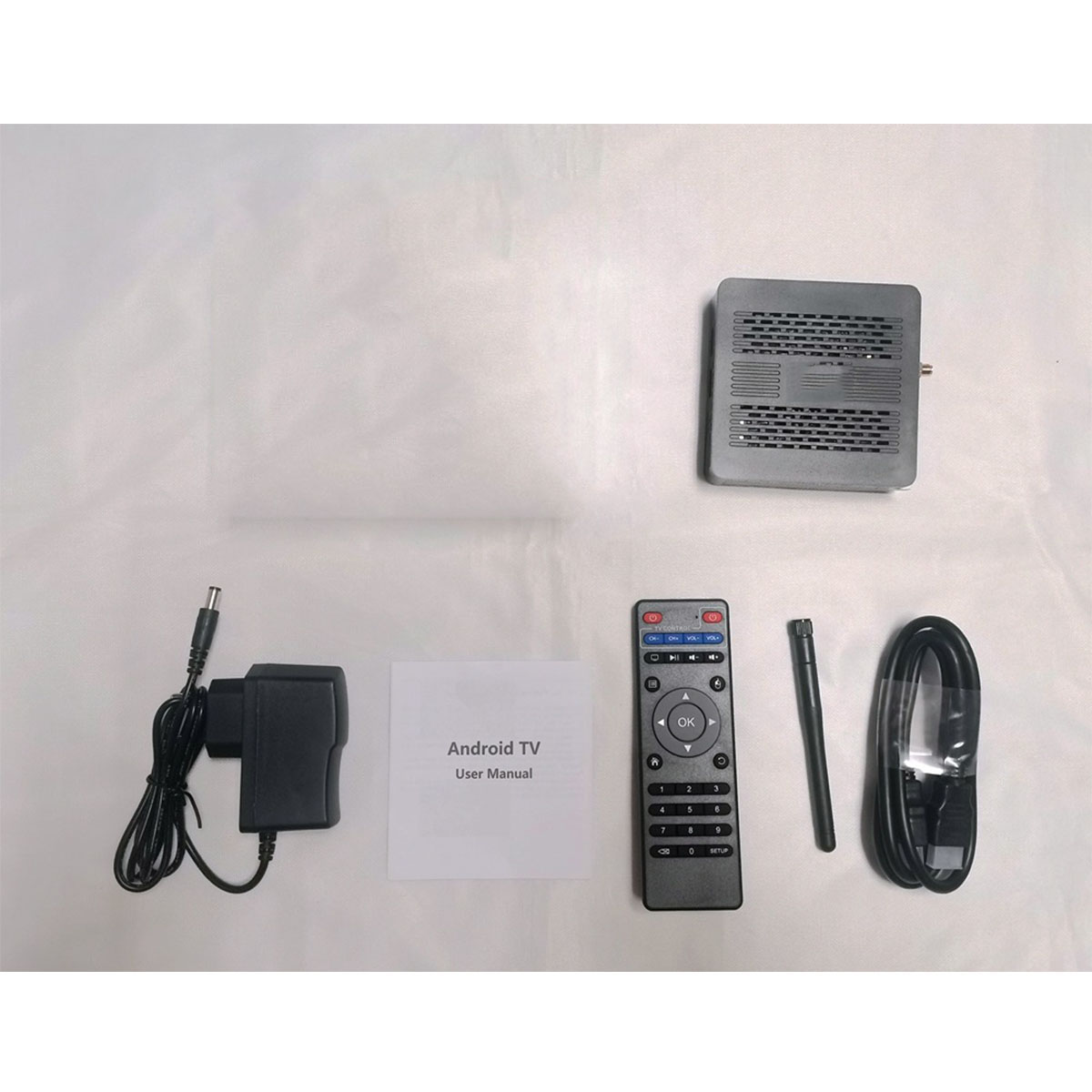 Eine Android TV Box mit Zubehör. Enthält Fernbedienung, Netzteil, Handbuch und ein schwarzes Kabel.