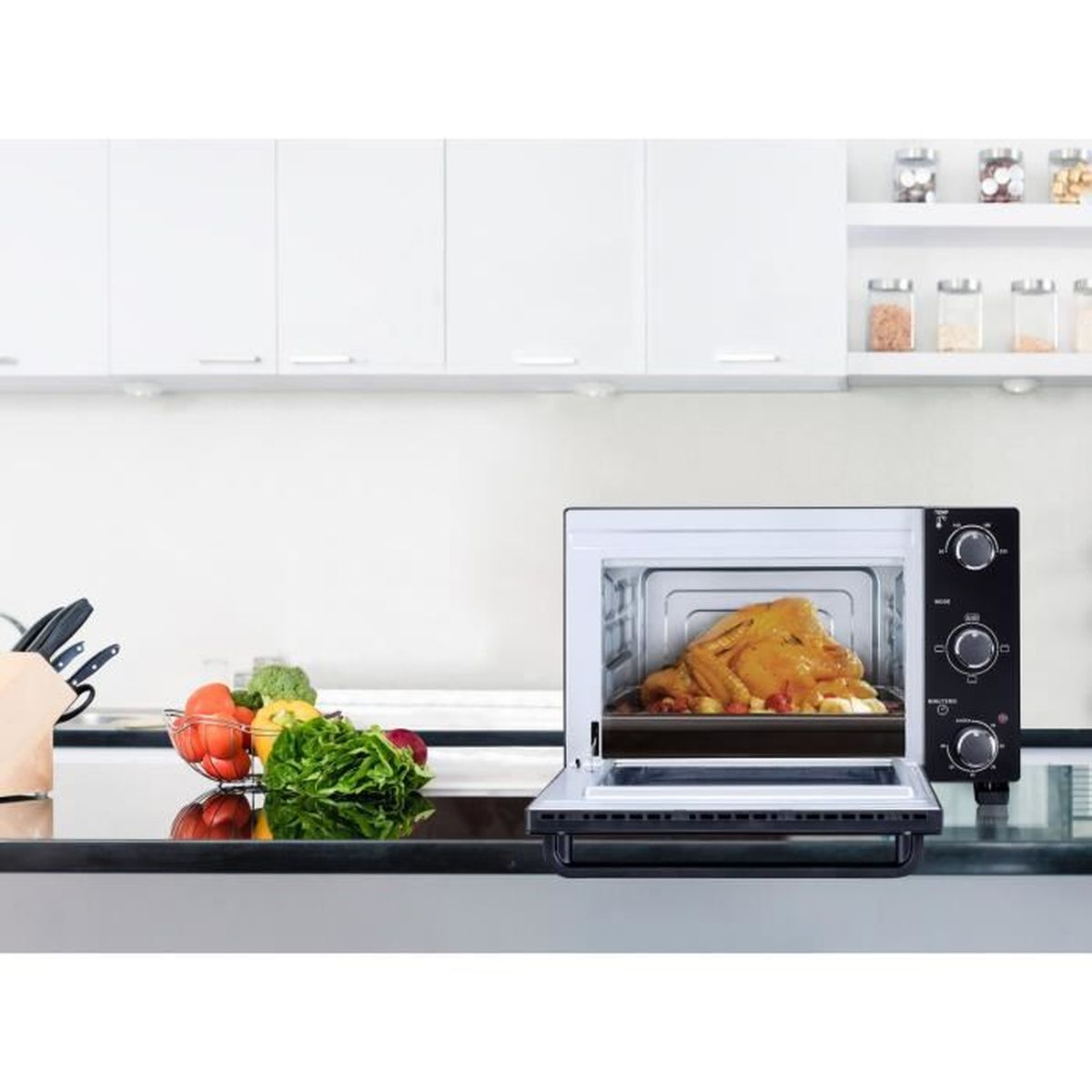 Un horno abierto mostrando pollo cocido. Cocina con gabinetes blancos, una encimera negra y algunas verduras.