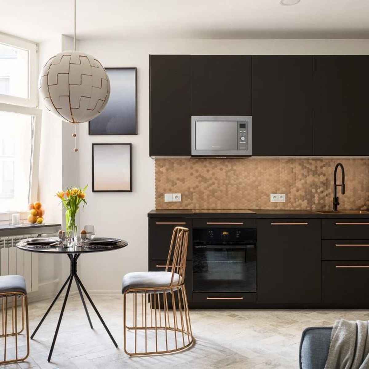 Een moderne keuken met zwarte kasten, een magnetron en een ronde tafel met bloemen.