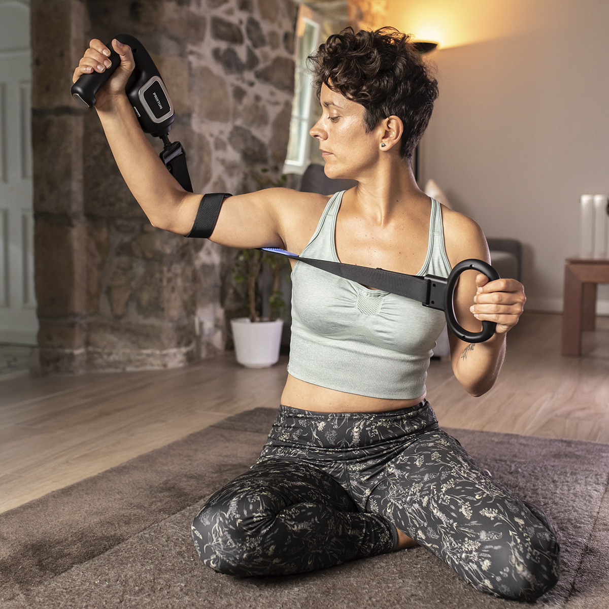 Kobieta ćwiczy z czarno-szarym urządzeniem do ćwiczeń. Jest w pokoju z kamienną ścianą.