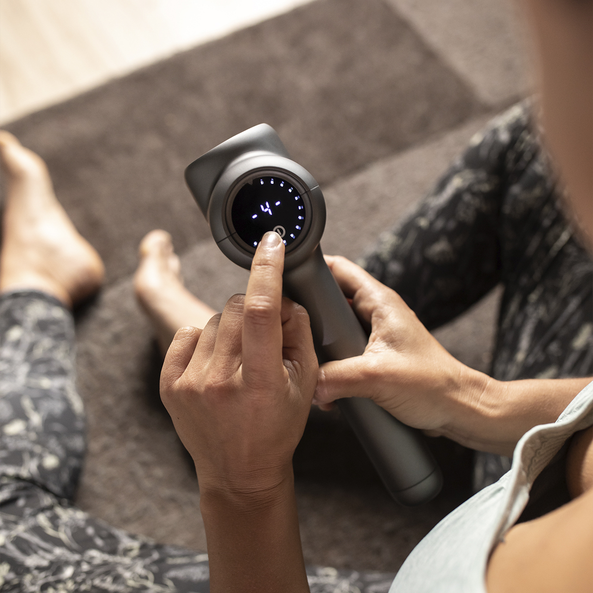 Osoba używa szarego pistoletu do masażu, naciskając przycisk.