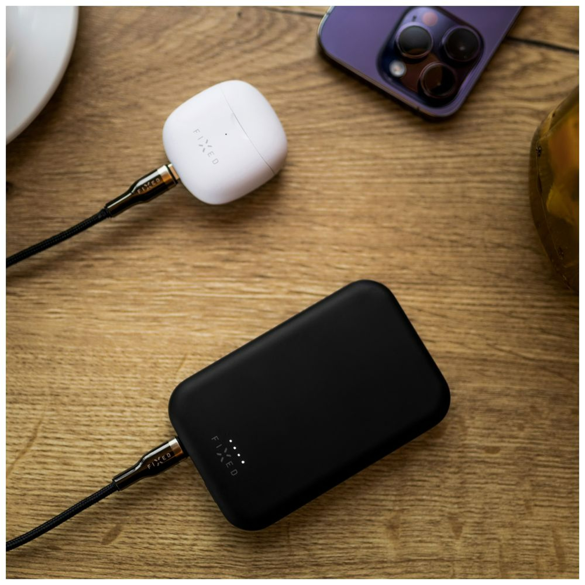 Weiße FIXED-Ohrhörer, die in einem weißen Ladeetui und einer schwarzen Powerbank aufgeladen werden.