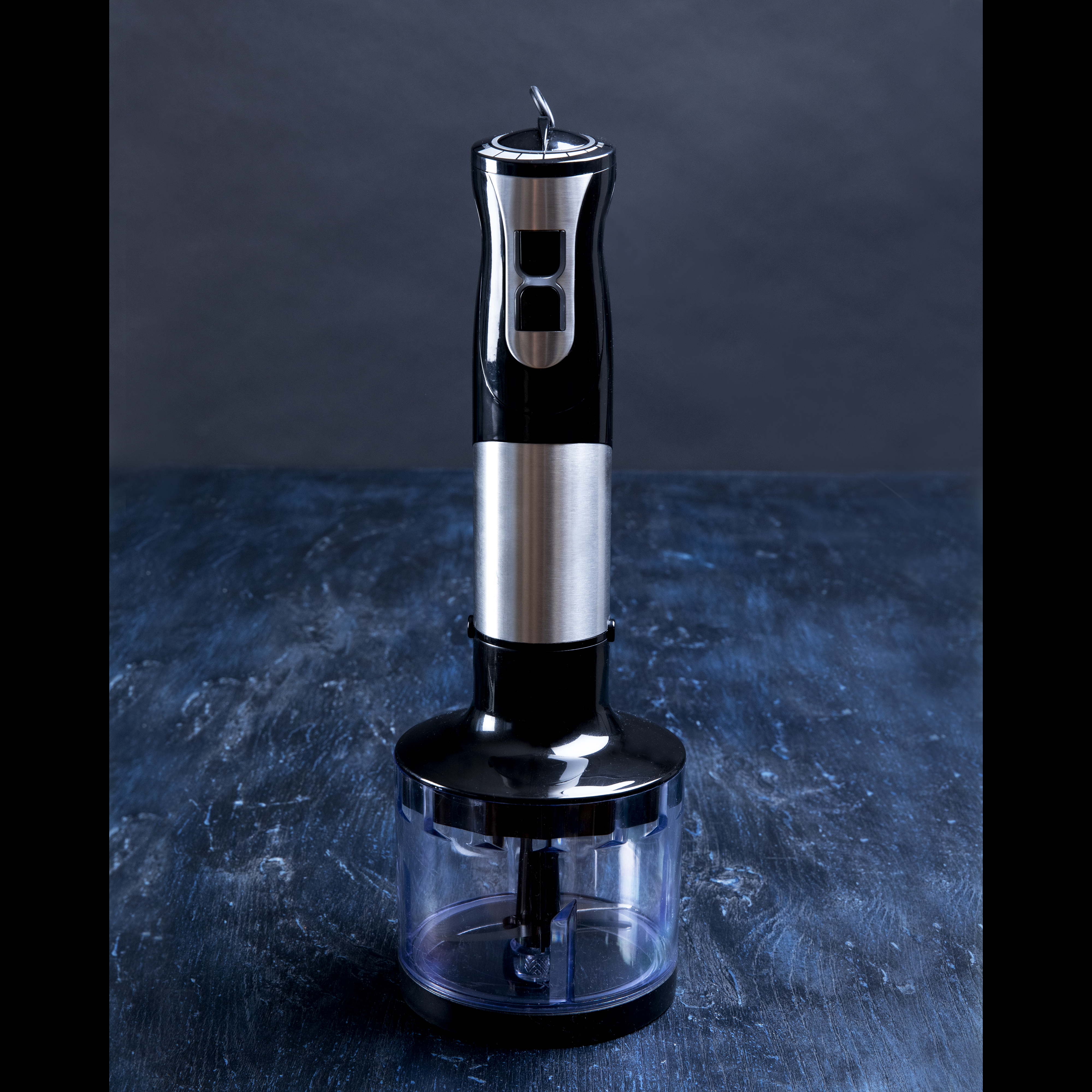 Czarny i srebrny blender ręczny na ciemnoniebieskiej, teksturowanej powierzchni, na tle ciemnoniebieskiego tła.