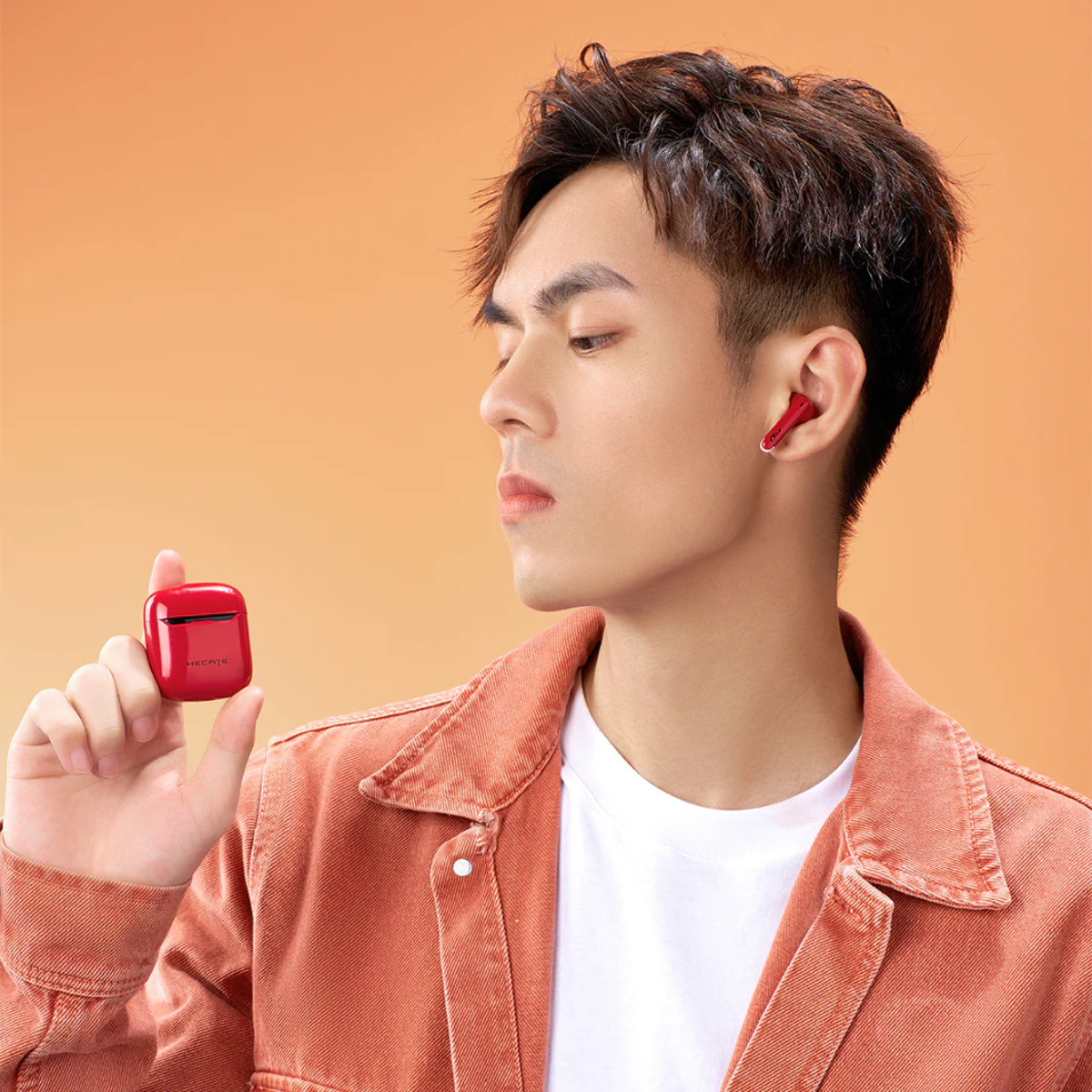 Uomo che tiene auricolari wireless rossi. Un auricolare nell'orecchio. Sfondo arancione.