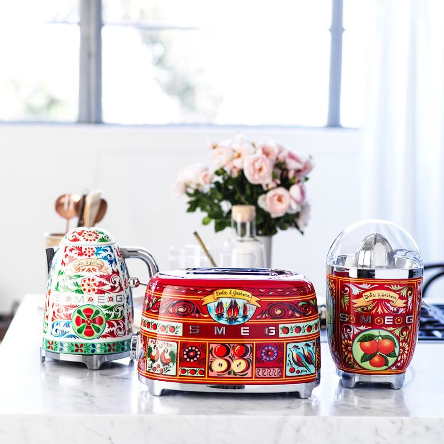 Eine Küchenszene mit farbenfrohen Dolce & Gabbana-Geräten. Ein Toaster, Entsafter und Wasserkocher stehen auf der Theke.