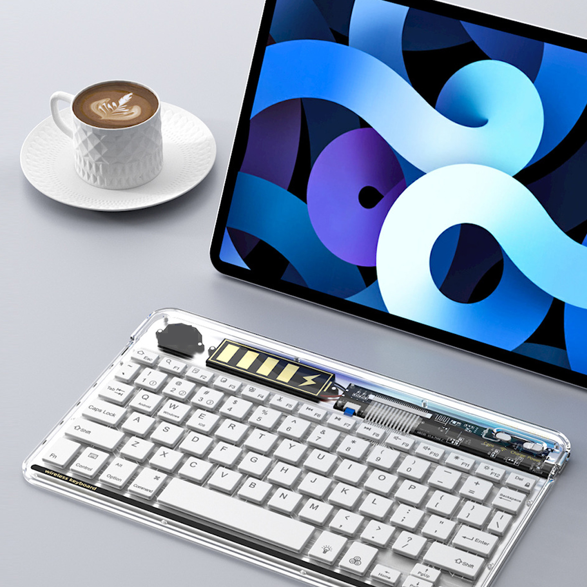 Transparente kabellose Tastatur. Tablet und Kaffee im Hintergrund. Batterieanzeige.