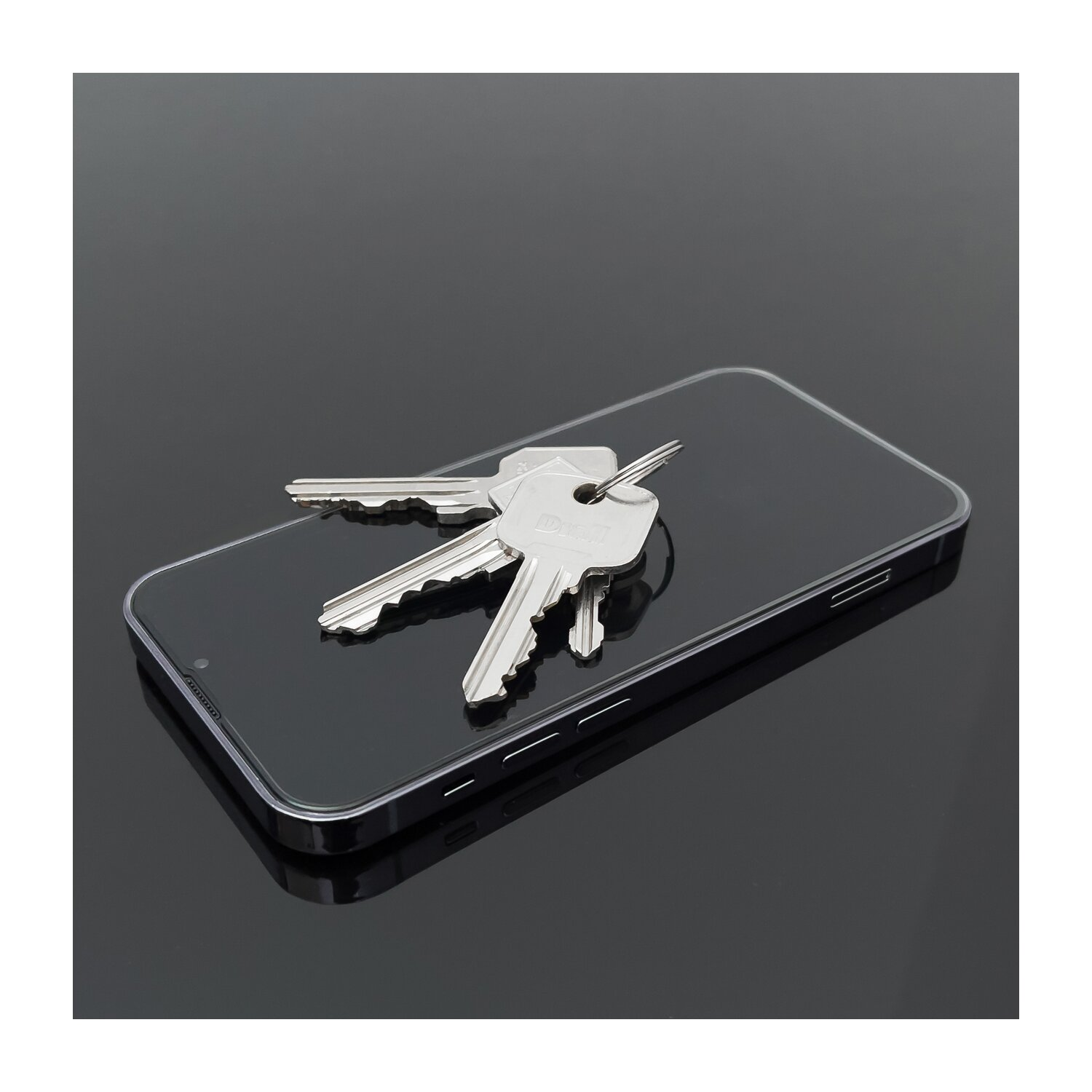 Ein Schlüsselbund liegt auf einem schwarzen Telefonbildschirm. Das Telefon befindet sich auf einer reflektierenden schwarzen Oberfläche.