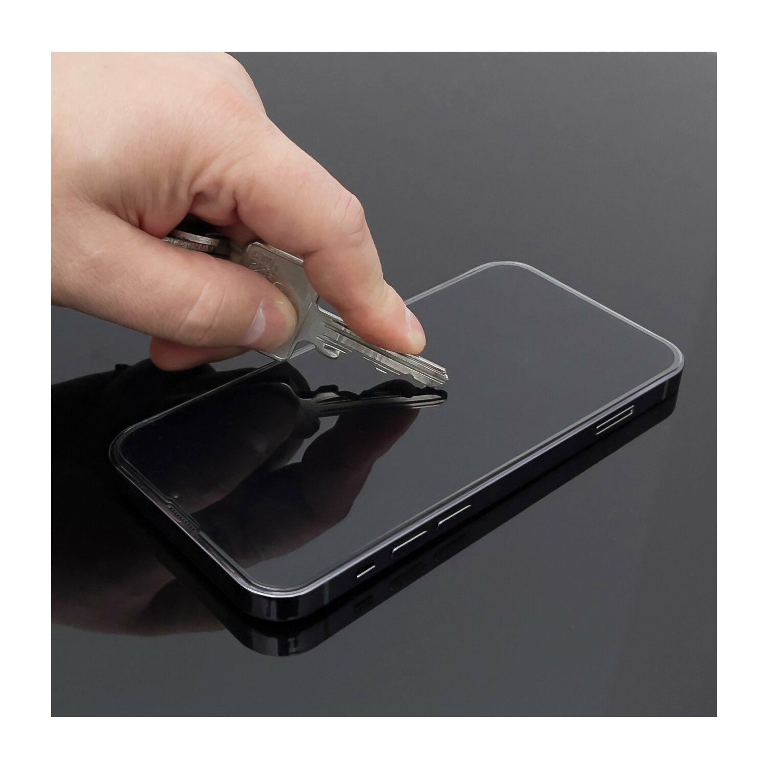 Eine Hand testet einen Displayschutz mit einem Schlüssel auf schwarzer Oberfläche.