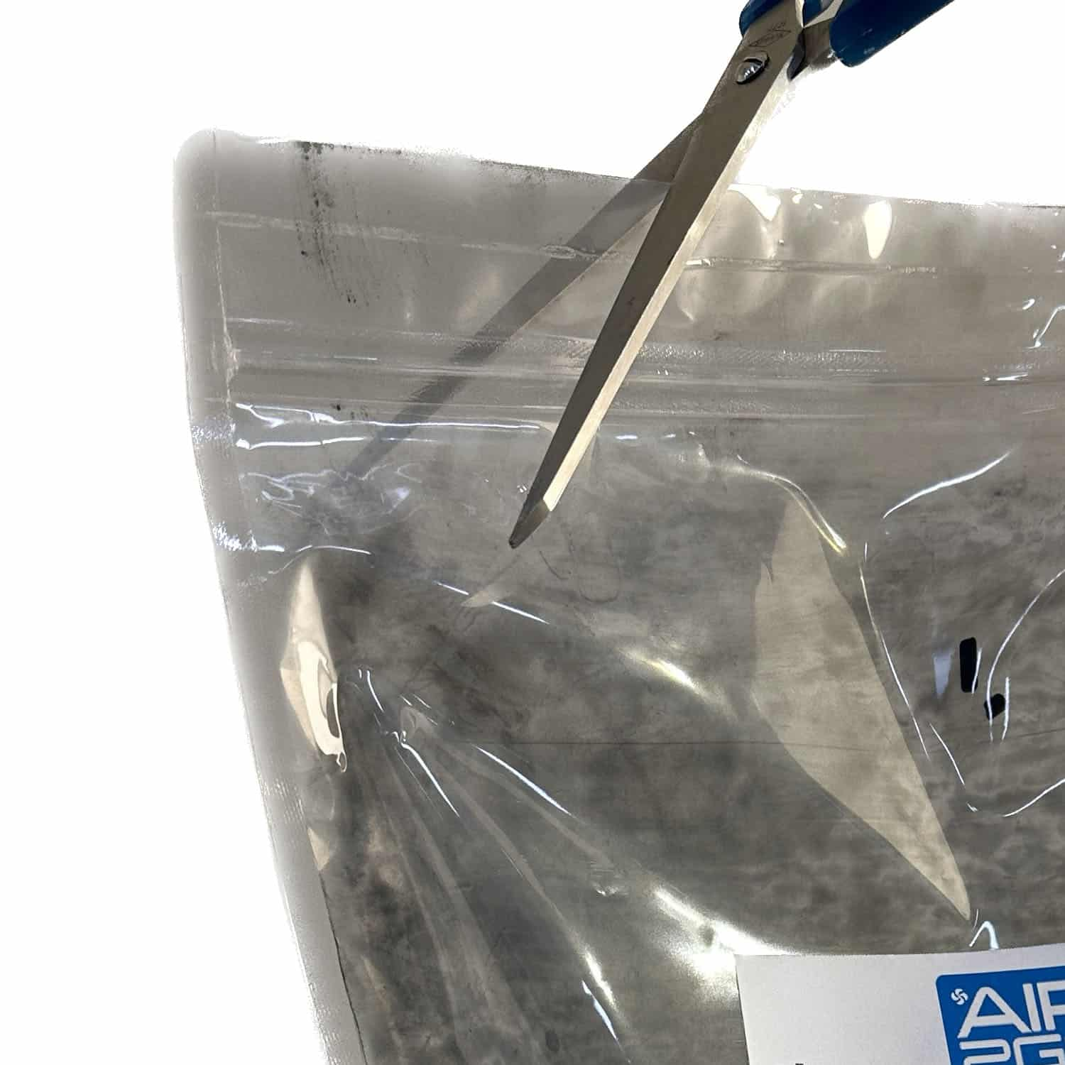 Schere schneidet eine Plastiktüte mit schwarzem Pulver. Weißer Hintergrund.