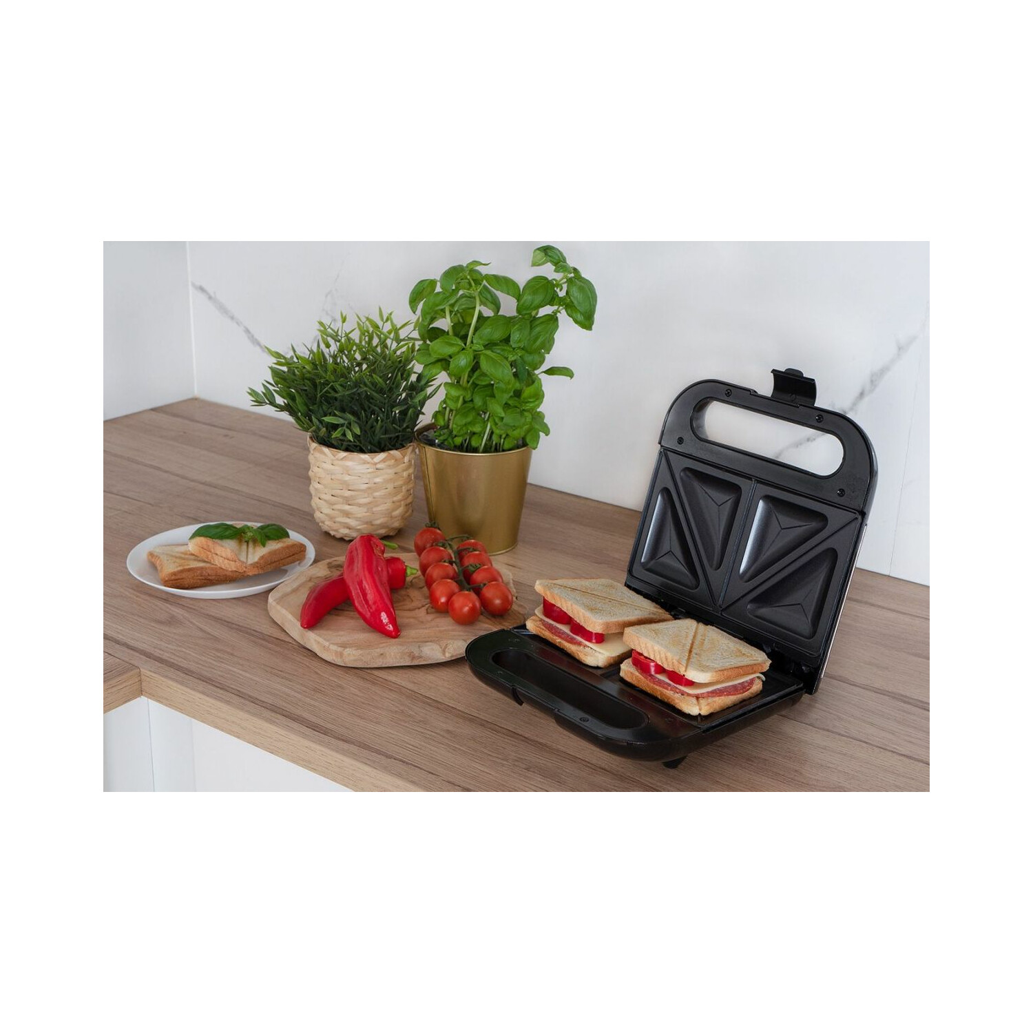 Sandwichmaker mit Sandwiches, Tomaten, Paprika, Basilikum und Pflanze auf Holzoberfläche.