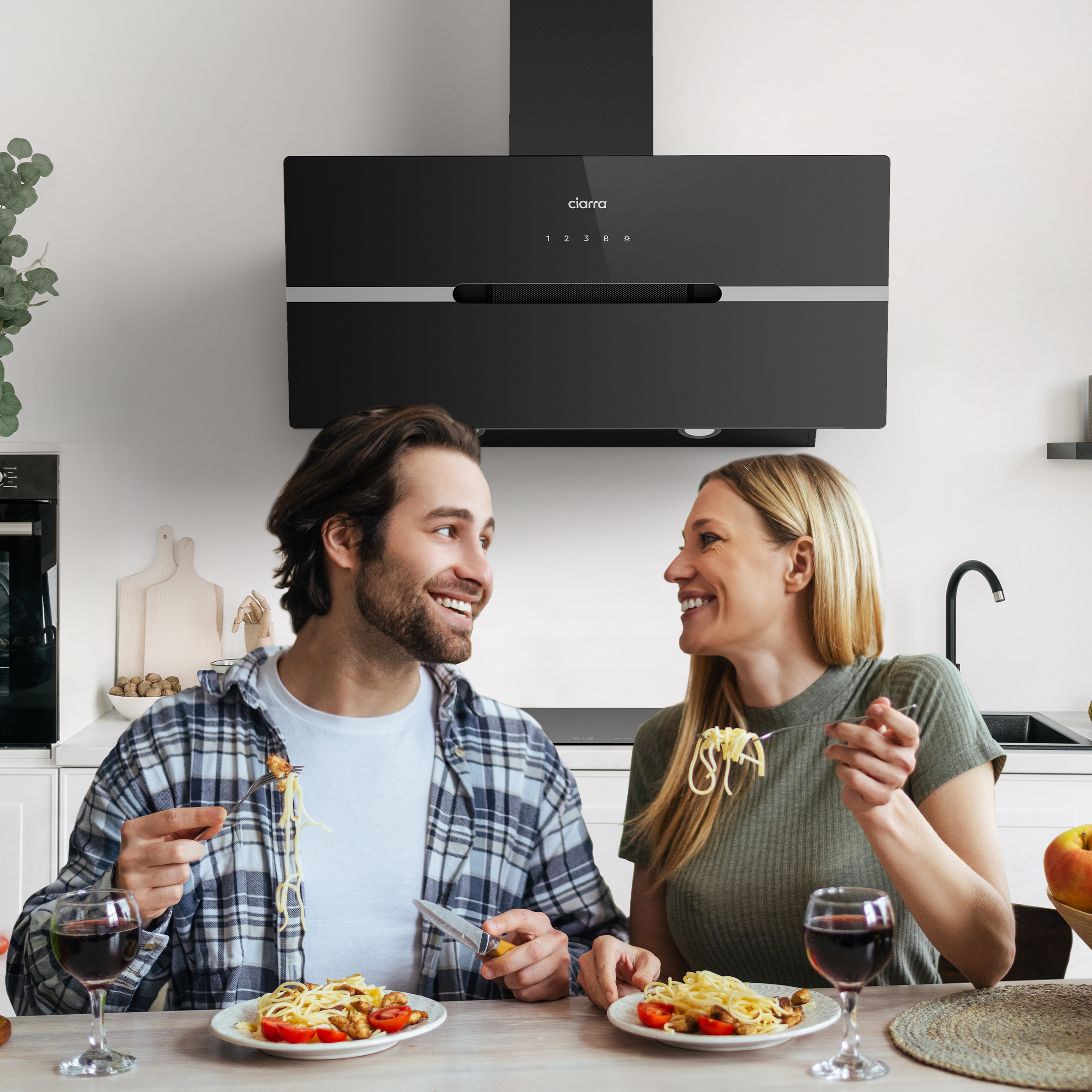 Koppel eet spaghetti in een keuken, zwarte afzuigkap erboven.