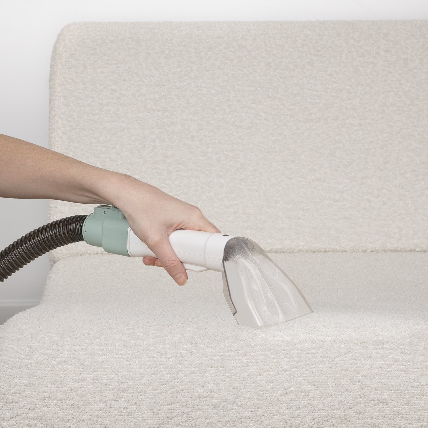 Una persona pulisce un divano di colore chiaro con un pulitore per tappezzeria portatile.