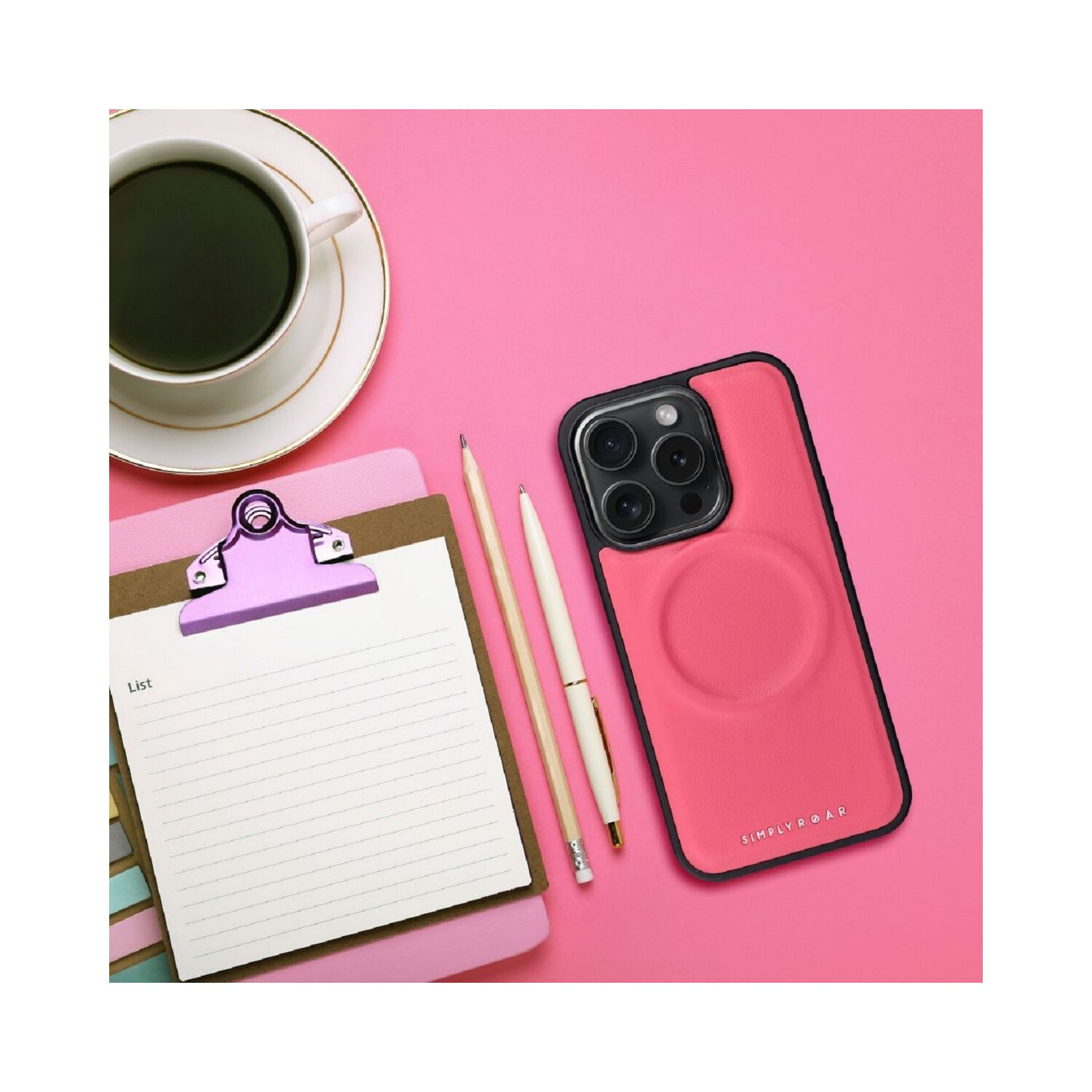 Una custodia per telefono rosa, un blocco appunti con un elenco, penne e una tazza di caffè su una superficie rosa.