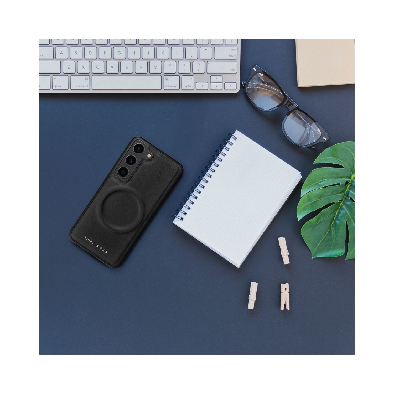 Arbeitsplatz mit Telefon in einer Hülle, Tastatur, Notizbuch, Brille und Klammern. Blaue Oberfläche.