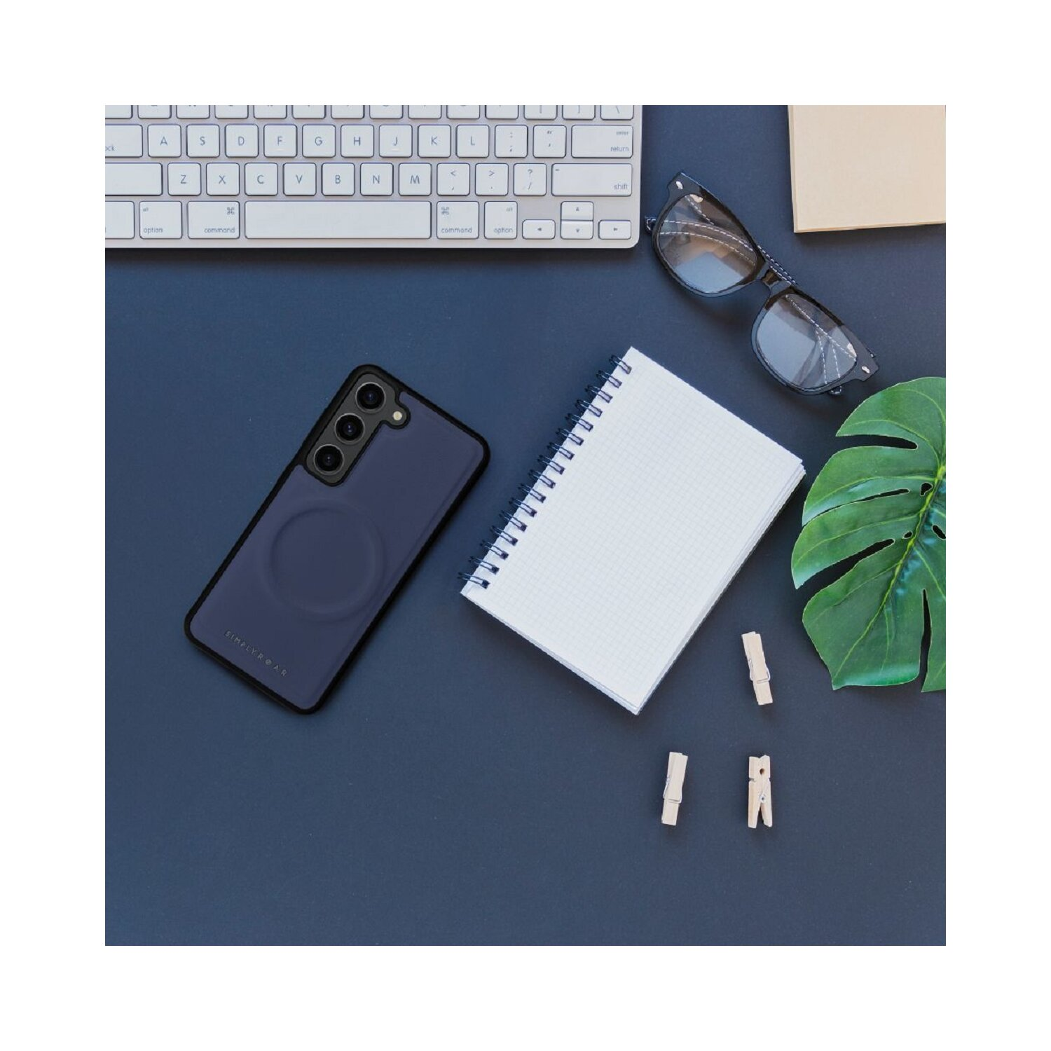 Schreibtisch mit Telefon, Tastatur, Notizbuch, Brille und Klammern auf dunkelblauem Grund.
