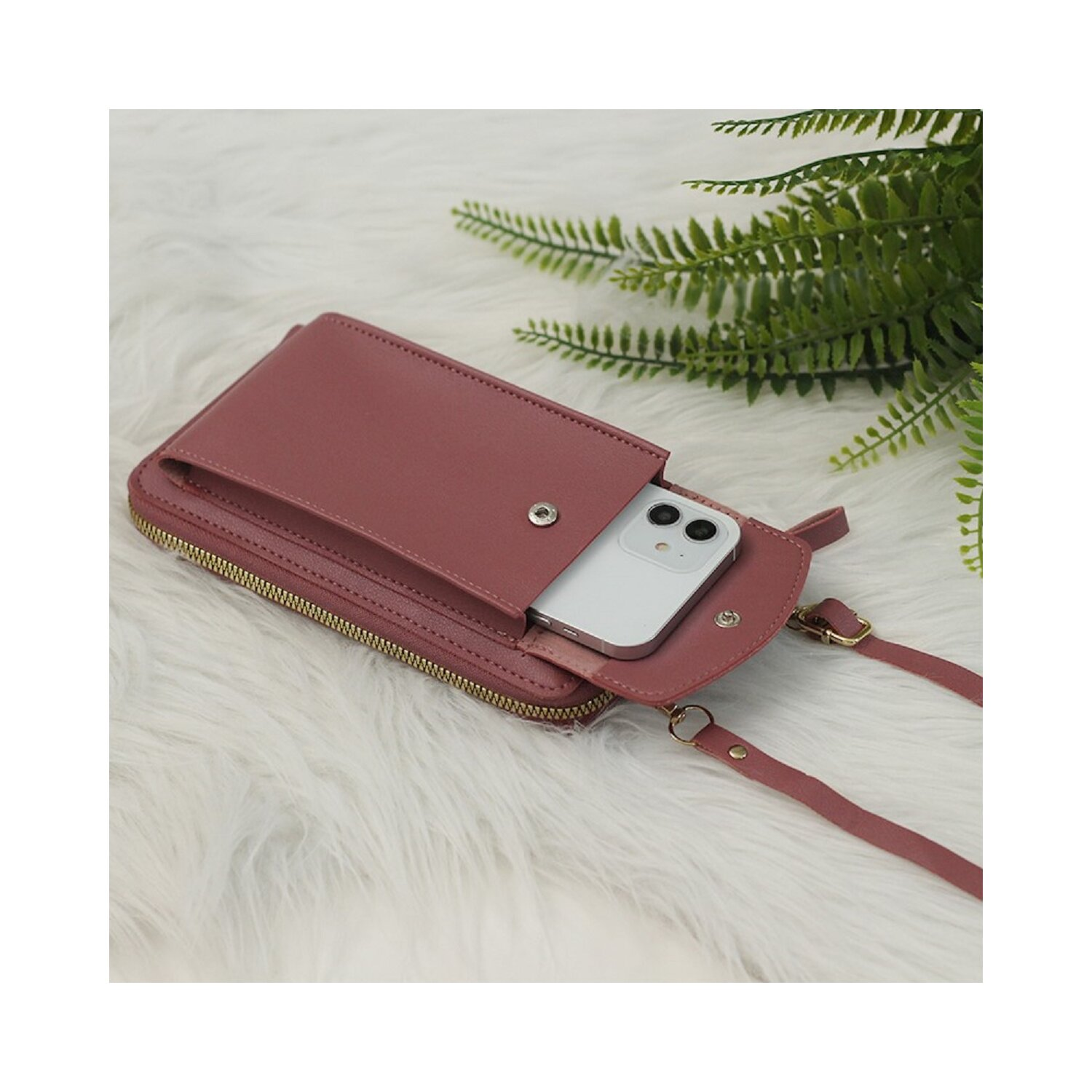 Ein pinkfarbenes Telefon-Portemonnaie mit einem Telefon darin. Das Portemonnaie hat einen Reißverschluss und einen Riemen. Es liegt auf einer flauschigen weißen Oberfläche.