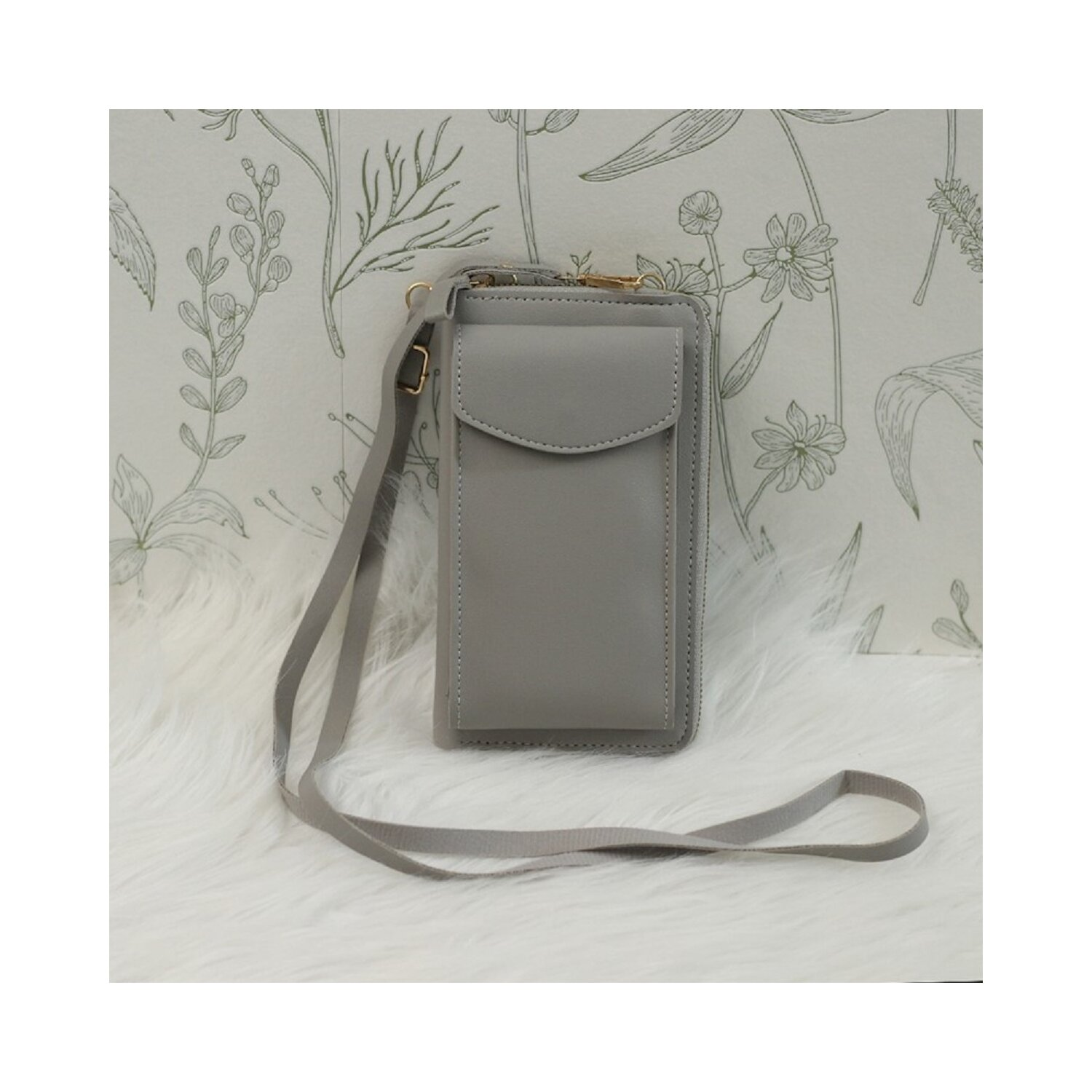 Graue Umhängetasche für Telefone mit Riemen. Die Tasche liegt auf einer weißen, fellartigen Oberfläche.