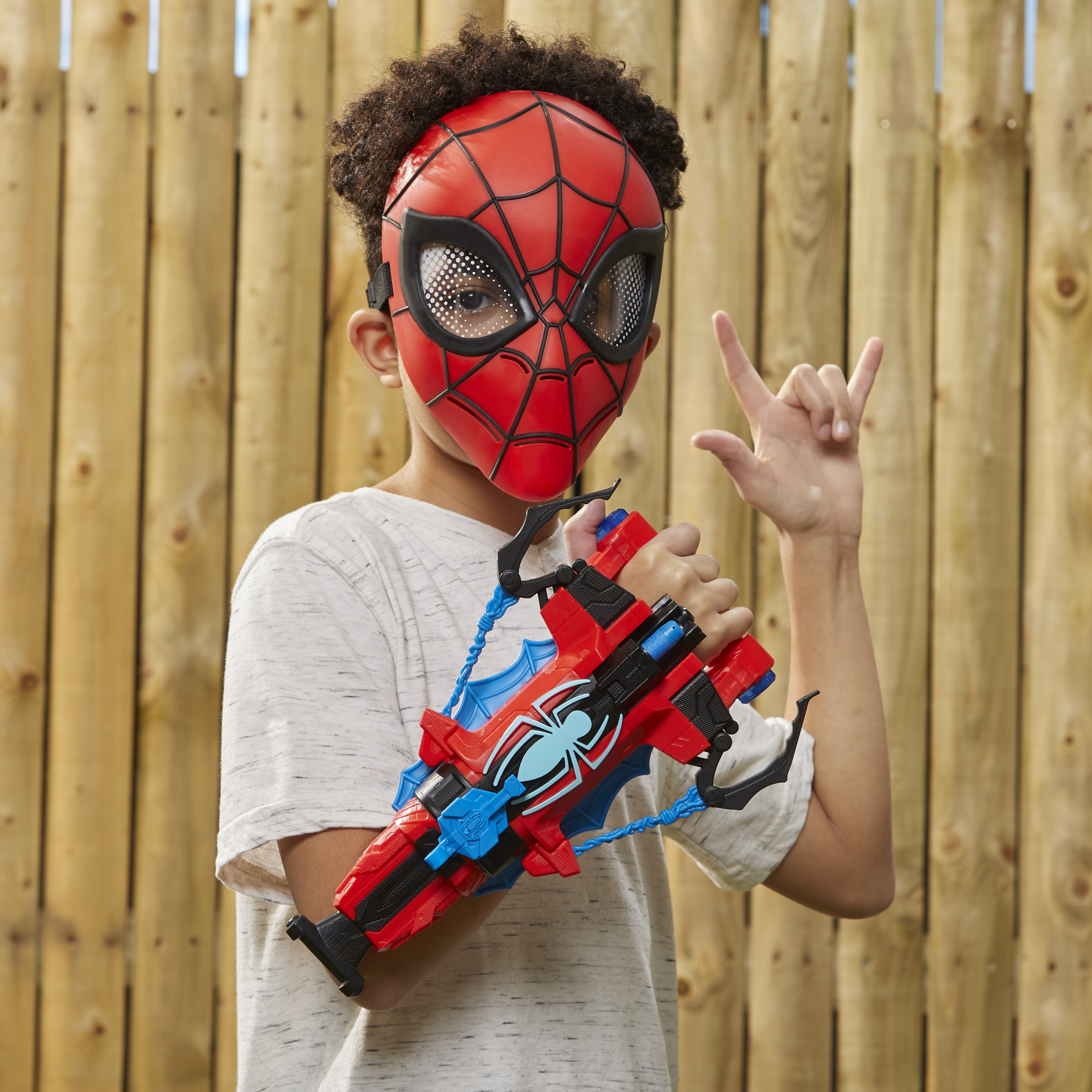 Un niño con una máscara de Spider-Man y un juguete lanzador de telarañas. Fondo de valla de madera.