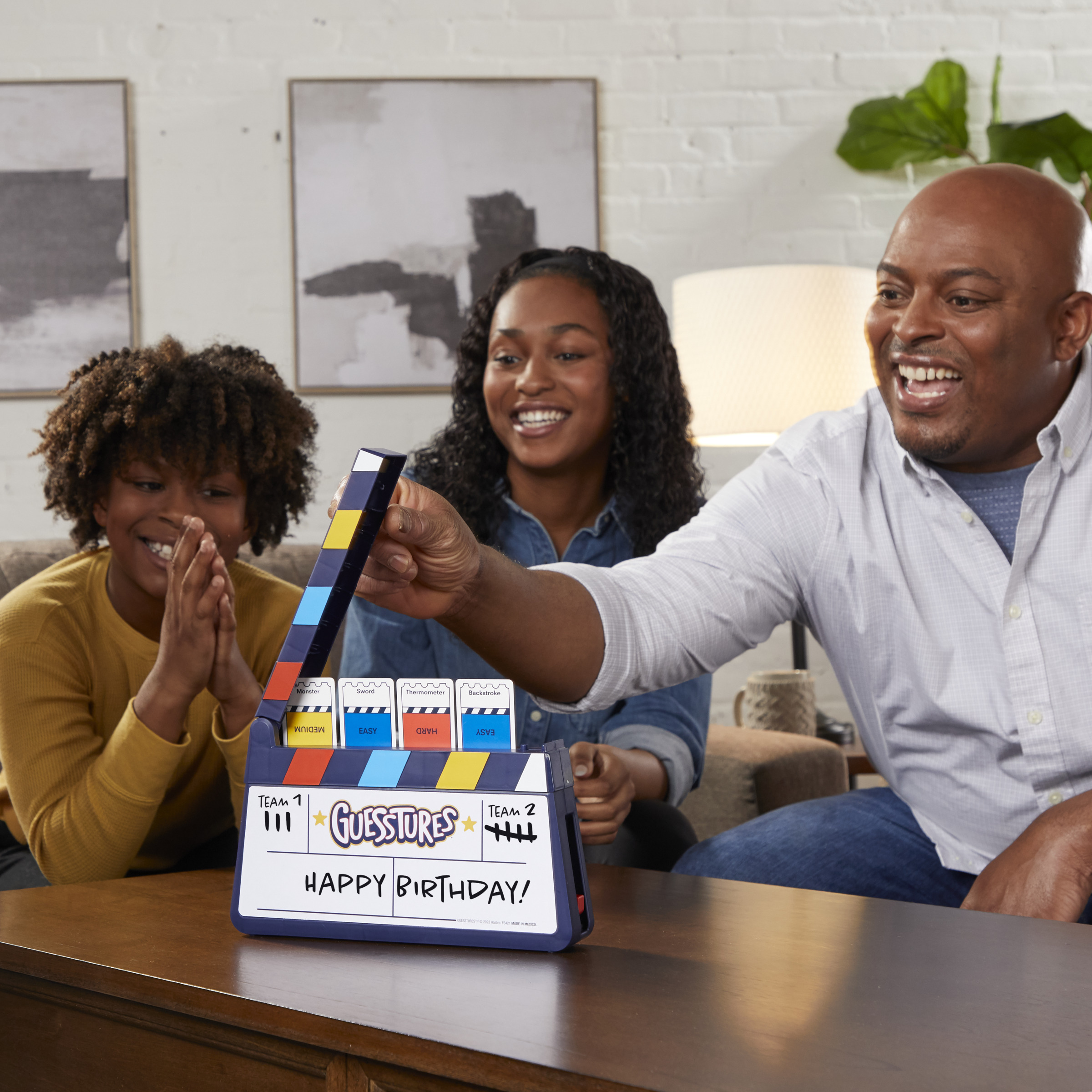 Familia jugando al juego ¿Quién es Quién?. El juego muestra la frase '¡Feliz Cumpleaños!'.