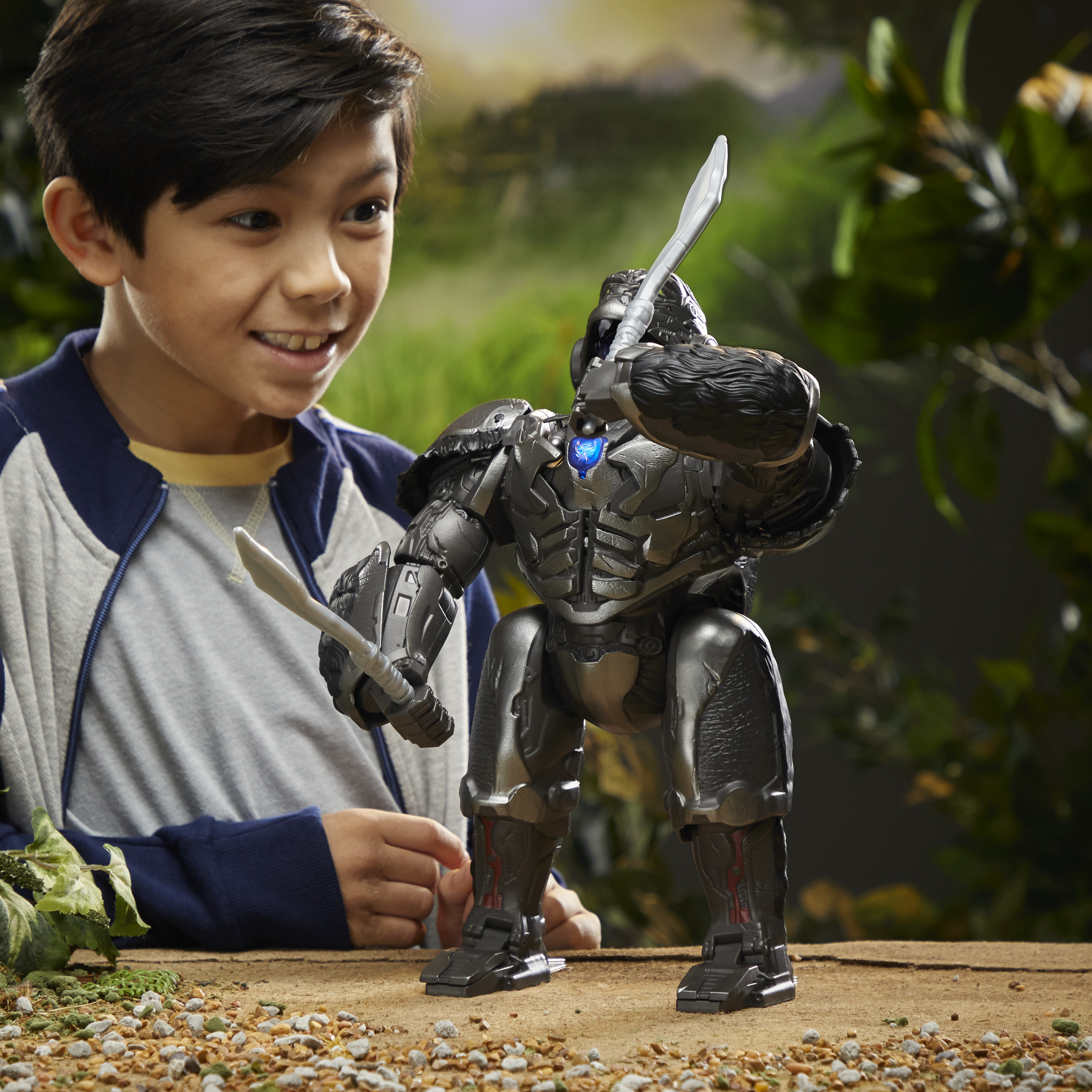 Młody chłopiec uśmiecha się do dużej, robotycznej zabawki goryla trzymającej miecze, z tłem dżungli.