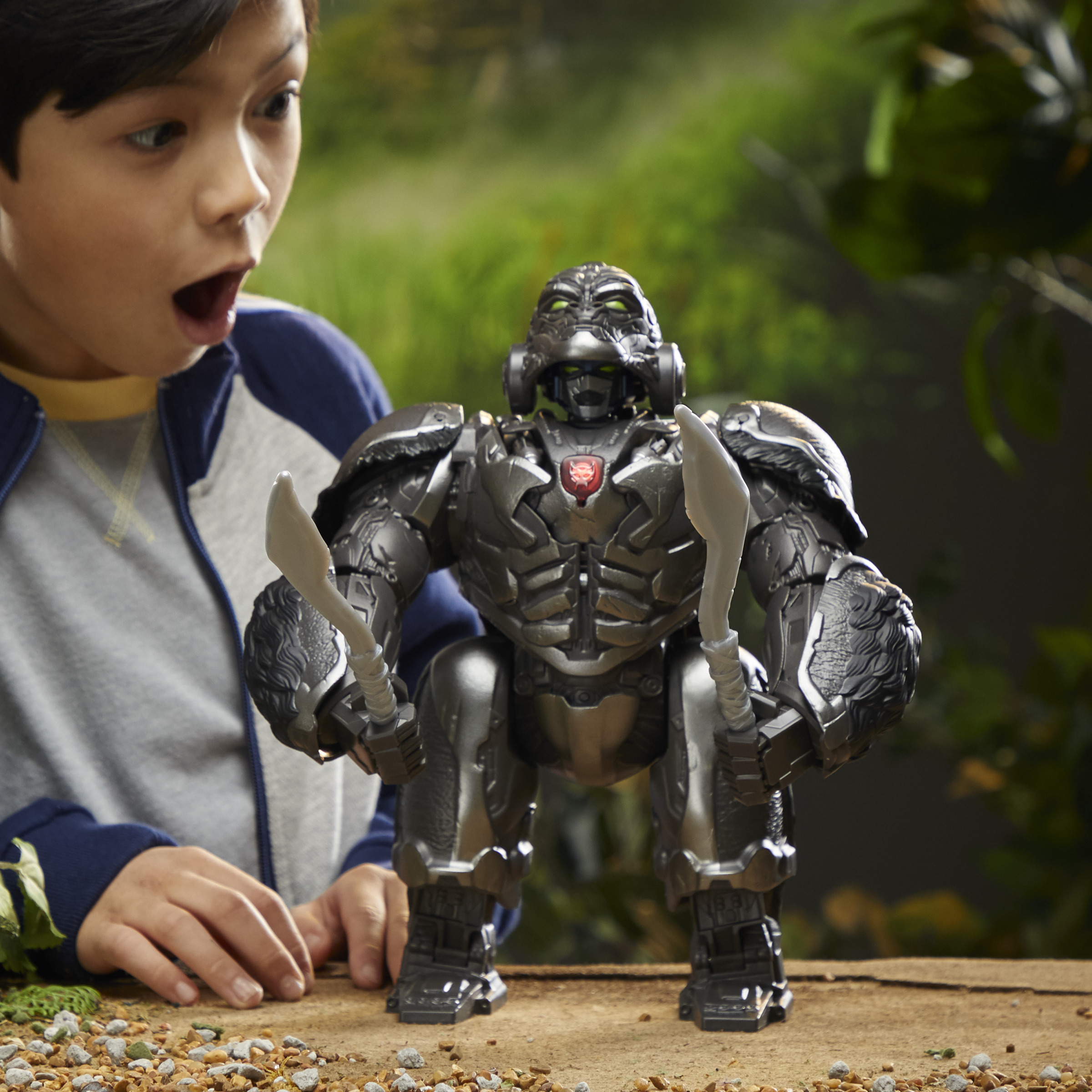 Dziecko zaskoczone zabawką robota z dwoma mieczami na tle lasu.