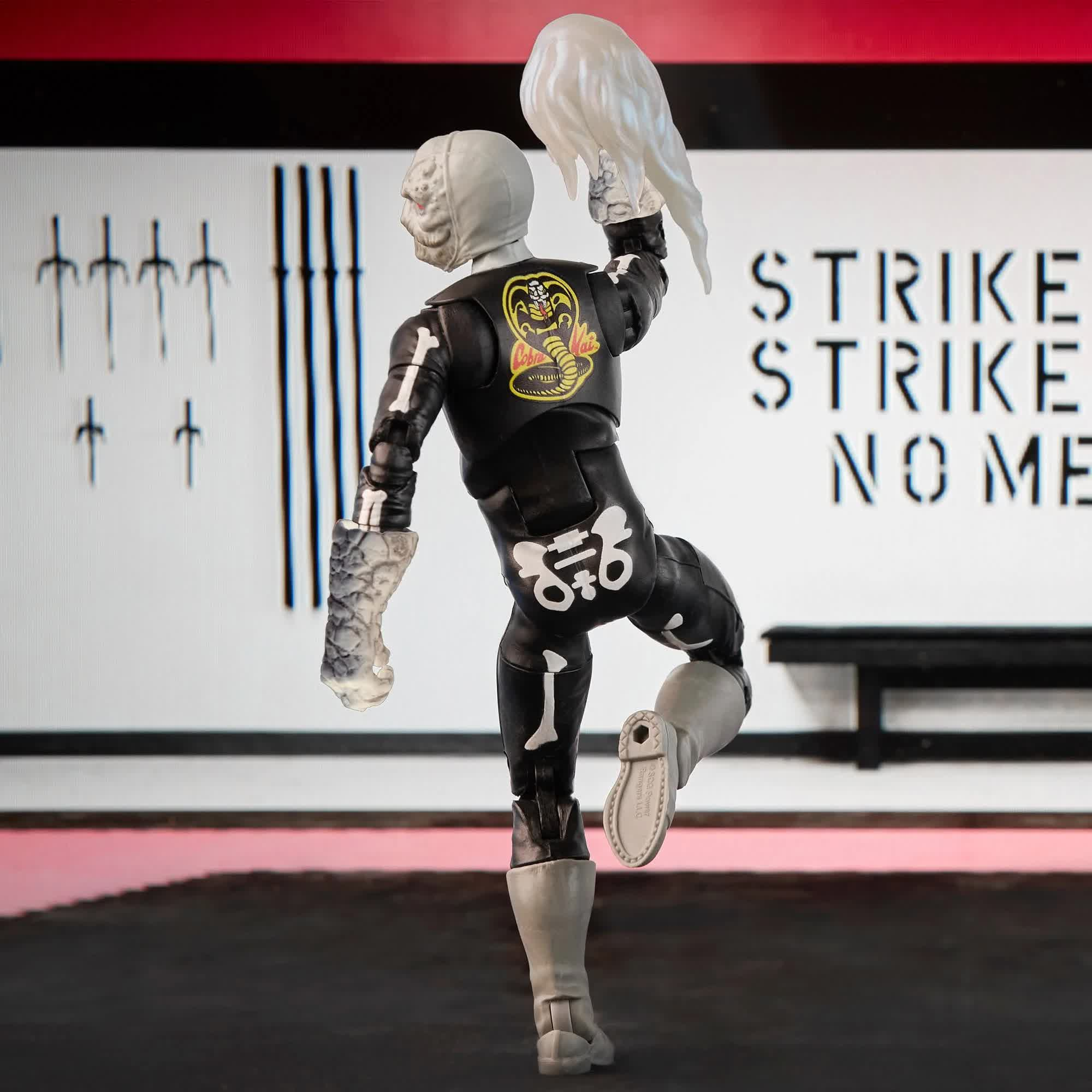 Figura de acción de Cobra Kai con traje de esqueleto, sosteniendo una cabeza. Fondo con espadas y texto.