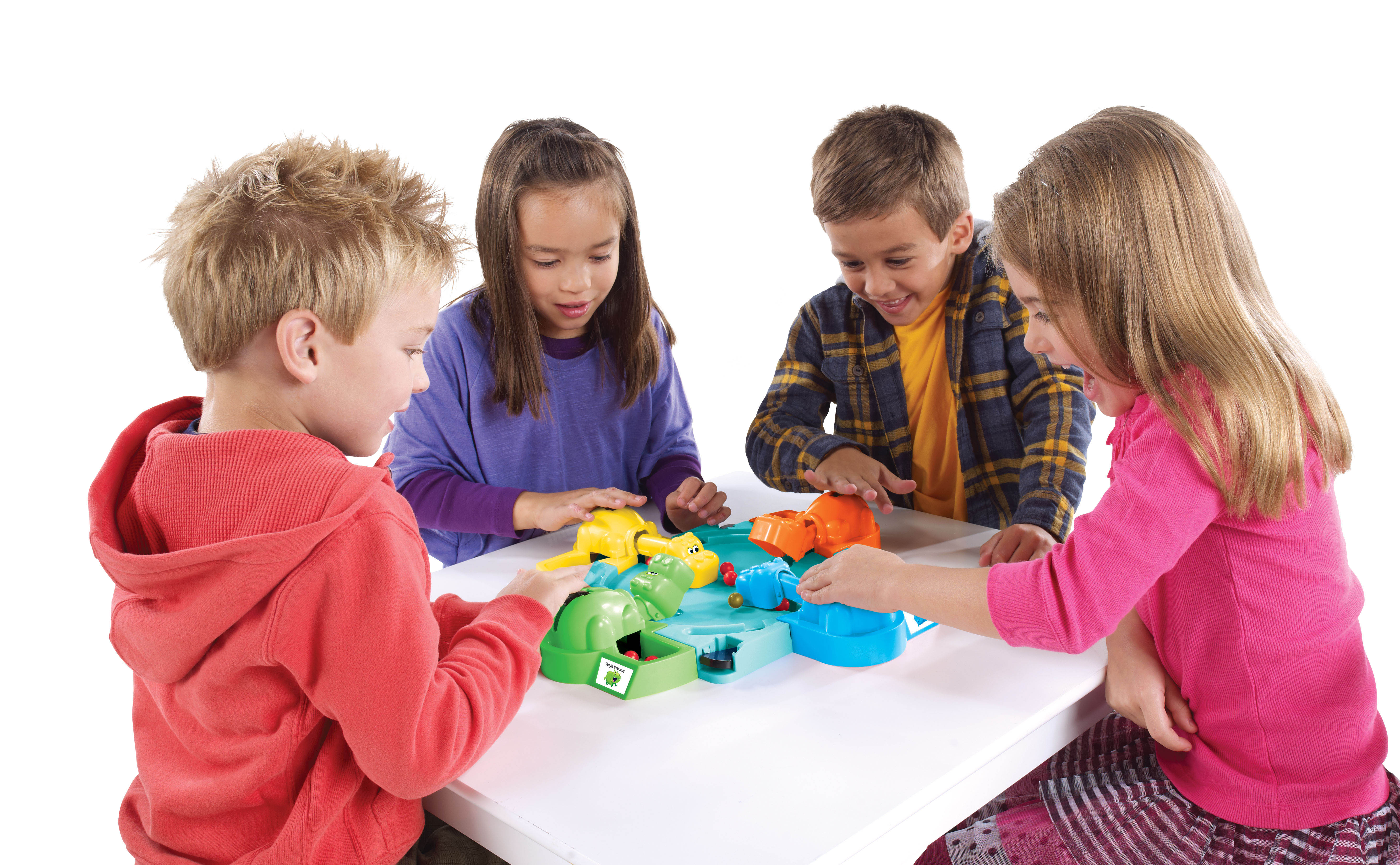 Cuatro niños jugando un juego de mesa alrededor de una mesa blanca; el juego tiene hipopótamos y una bandeja verde.