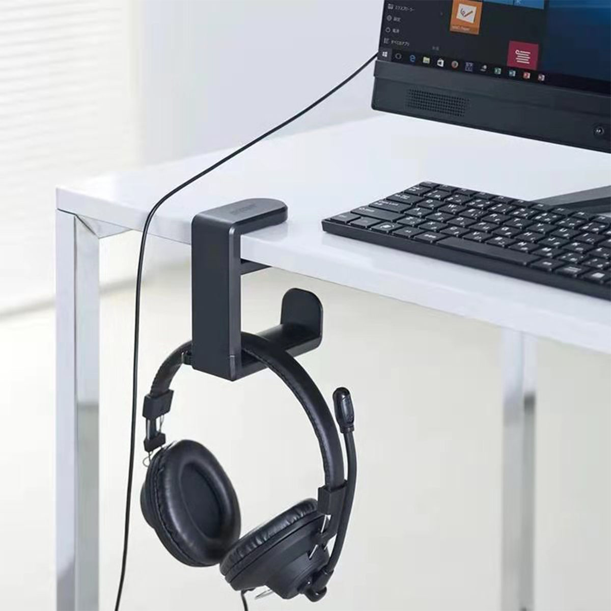 Kopfhörer hängen an einem Schreibtisch. Eine Computertastatur und ein Monitor sind im Hintergrund.